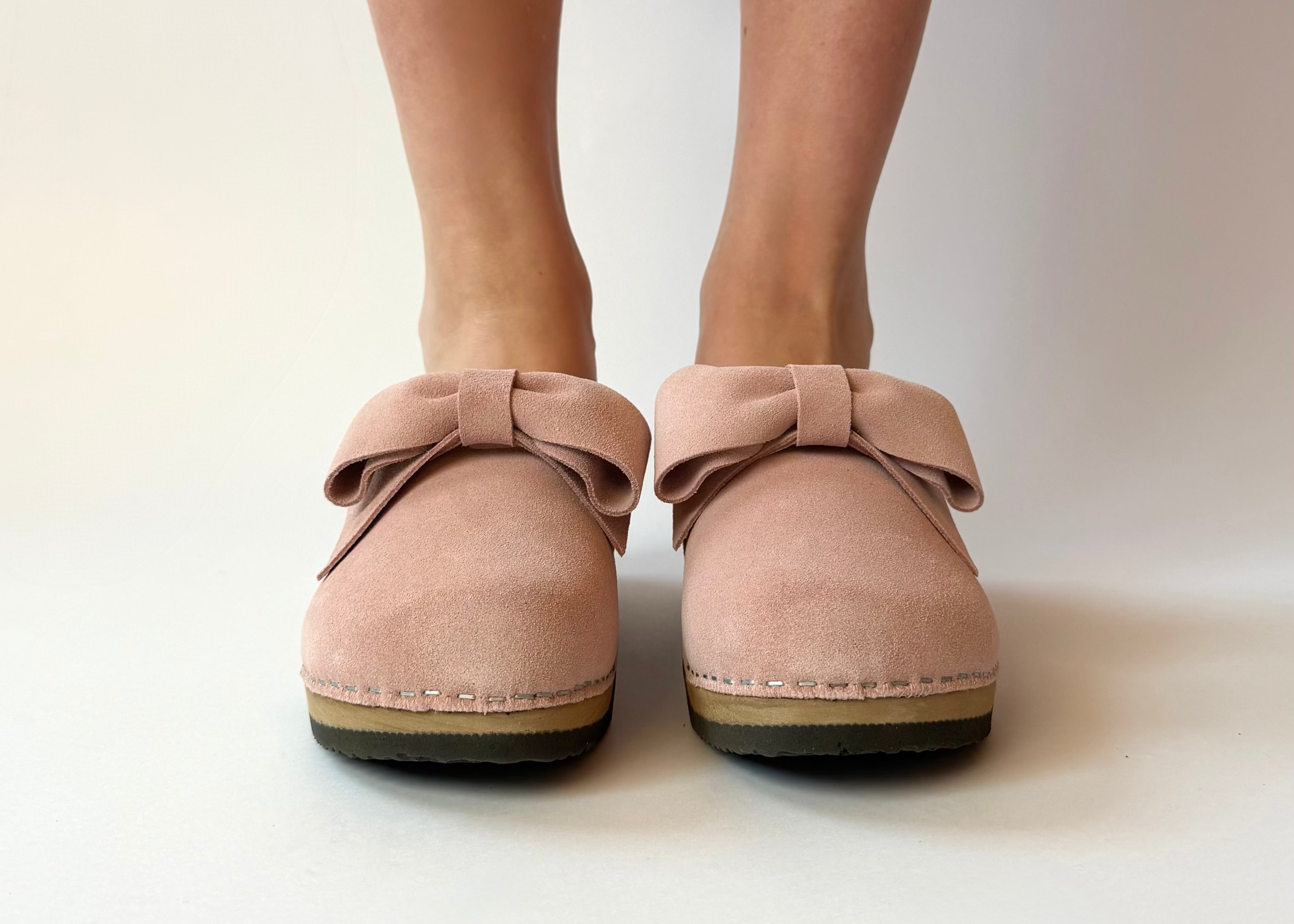 Pink clogs with bow details worn by a person on a white background