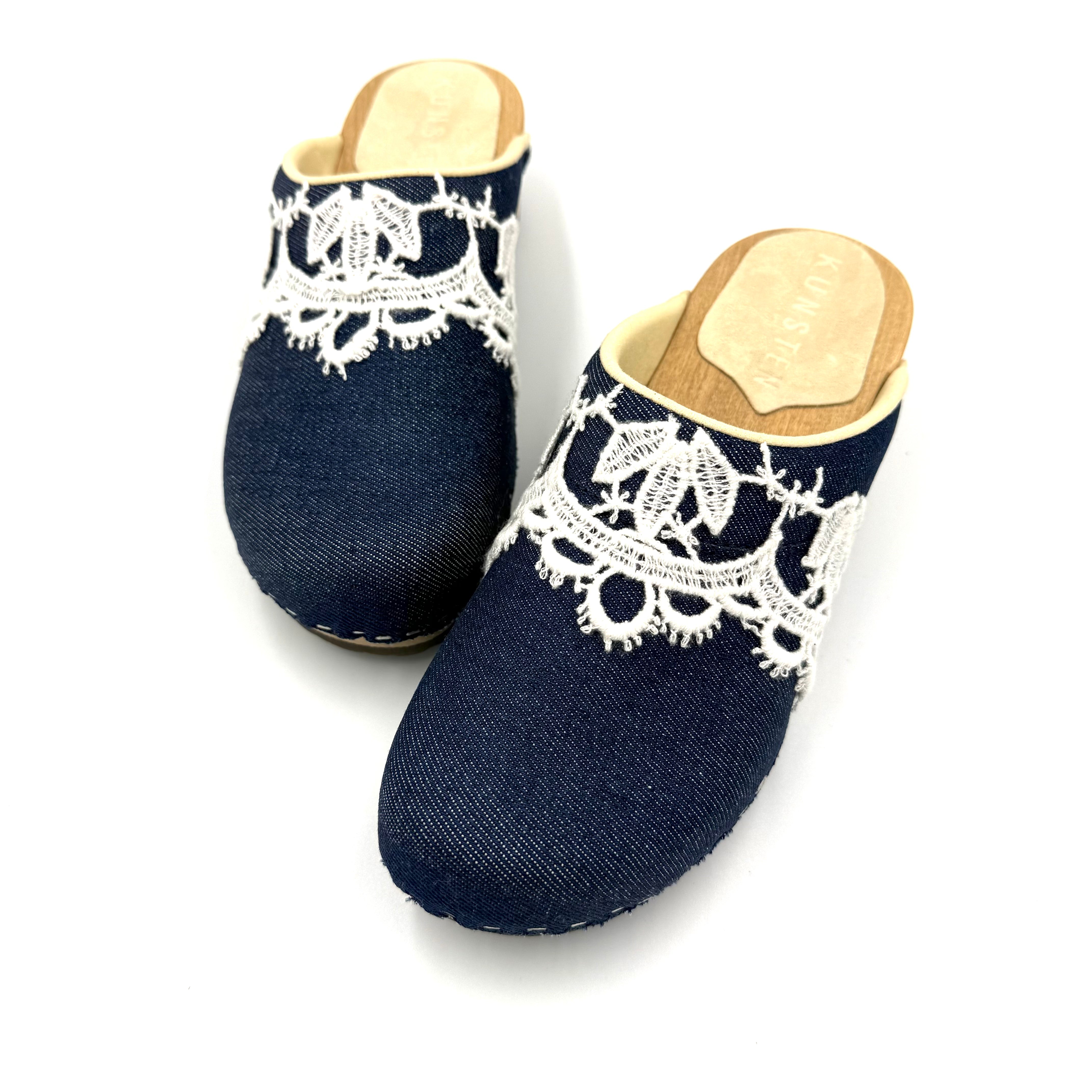 Pair of navy blue slippers with white lace details on a white background