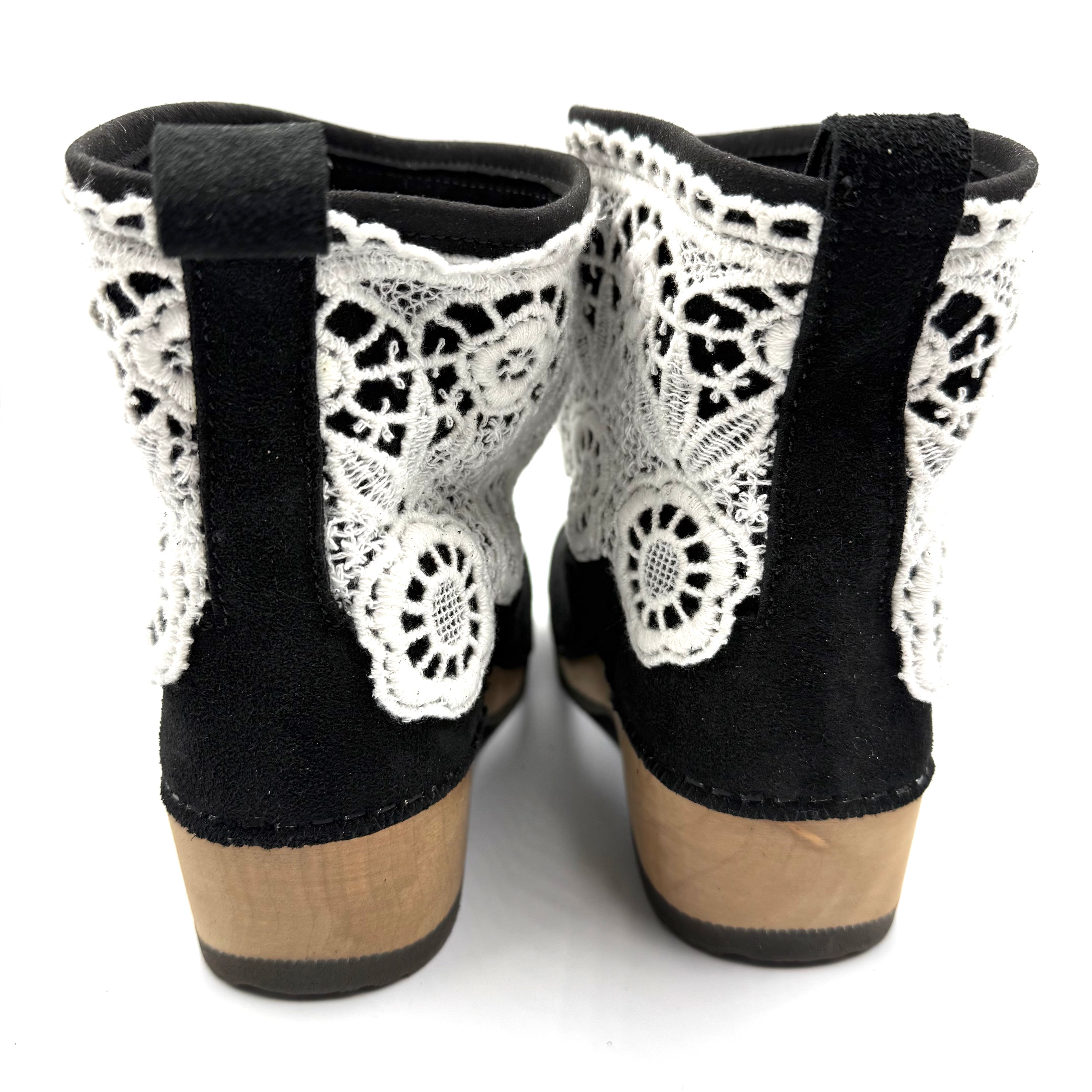 Black wedge sandals with white lace detailing on a white background