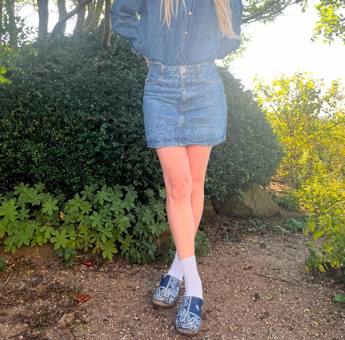 Person wearing a denim outfit with a skirt and shoes in a garden setting
