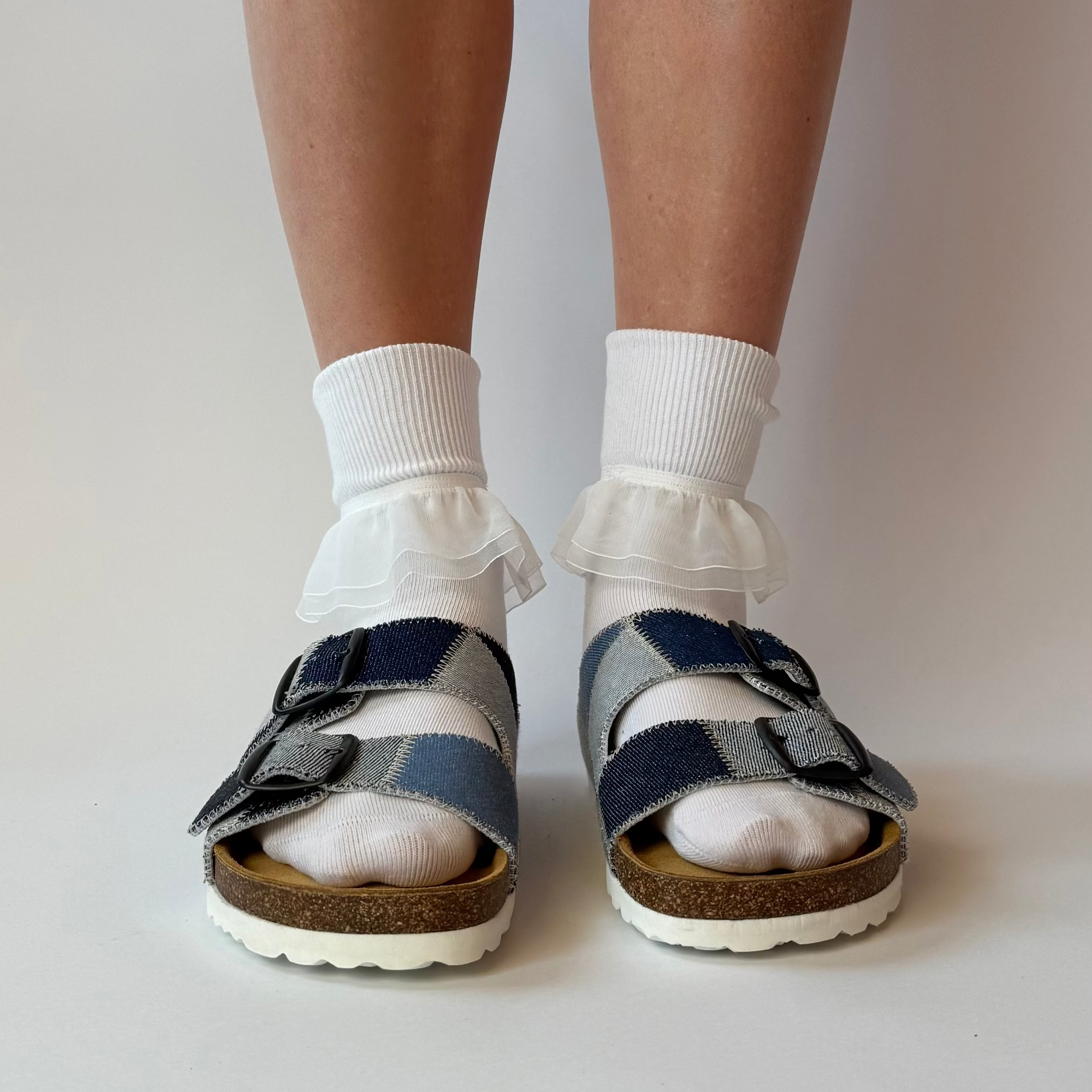 Person wearing blue and brown checkered sandals with white socks on a plain background