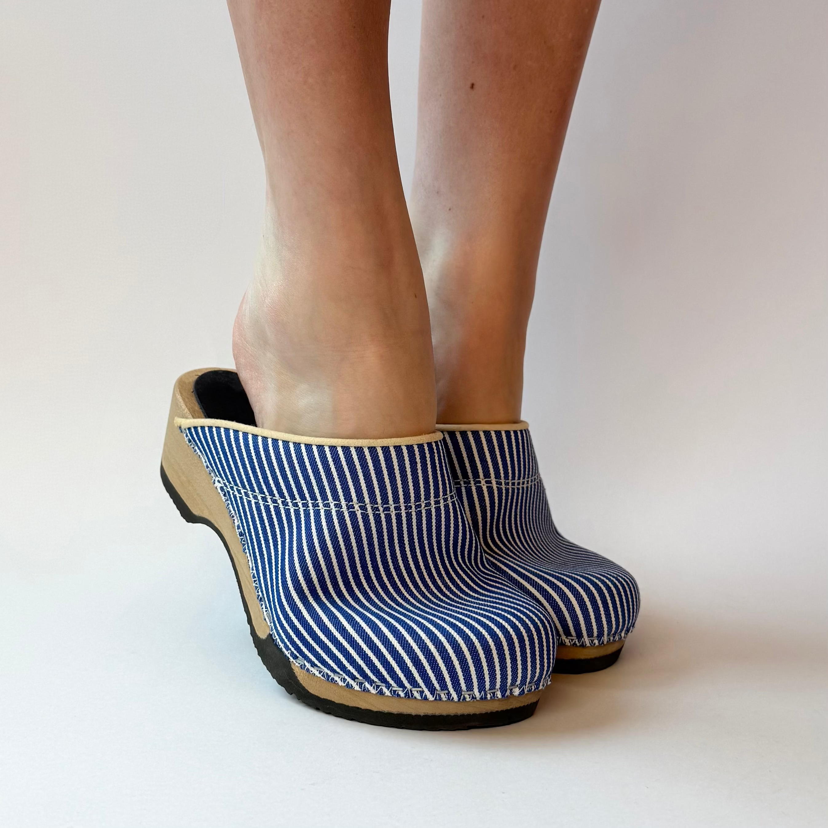 Blue striped clogs worn by a person on a white background