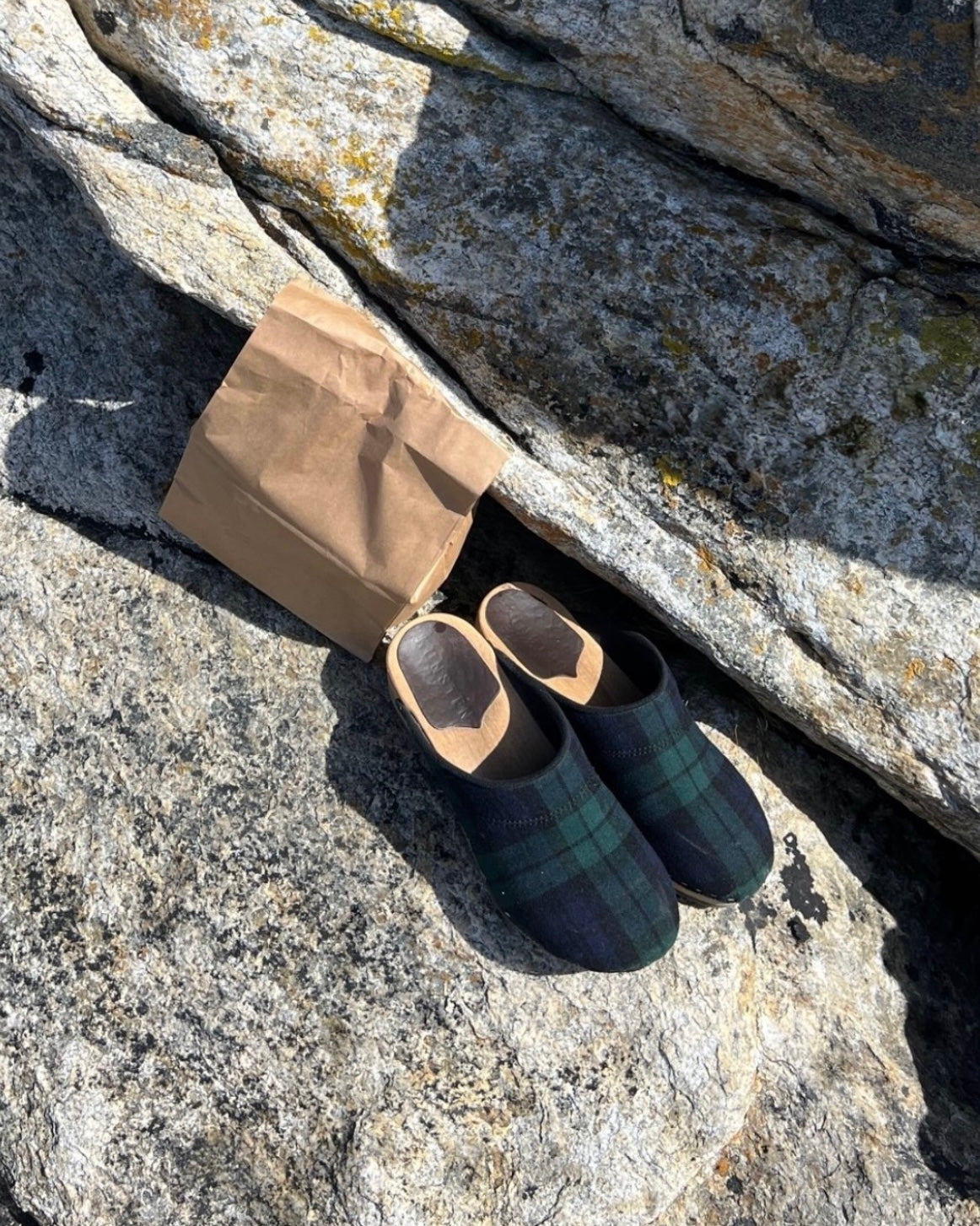 Embla clogs in Black Watch tartan wool on a bendable wooden sole, on sunlit granite