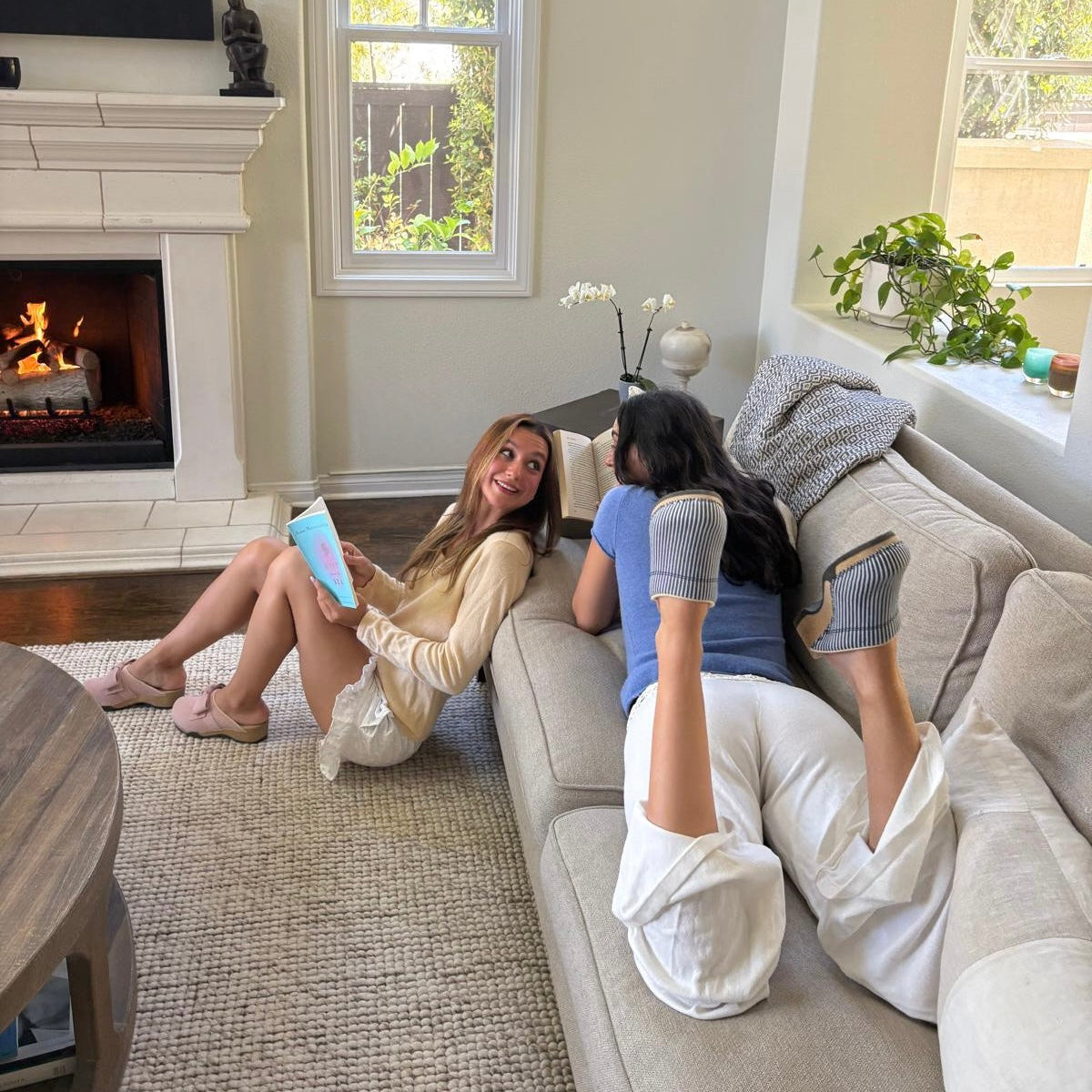 Two women relaxing on a couch by the fireplace wearing KUNSTEN clogs