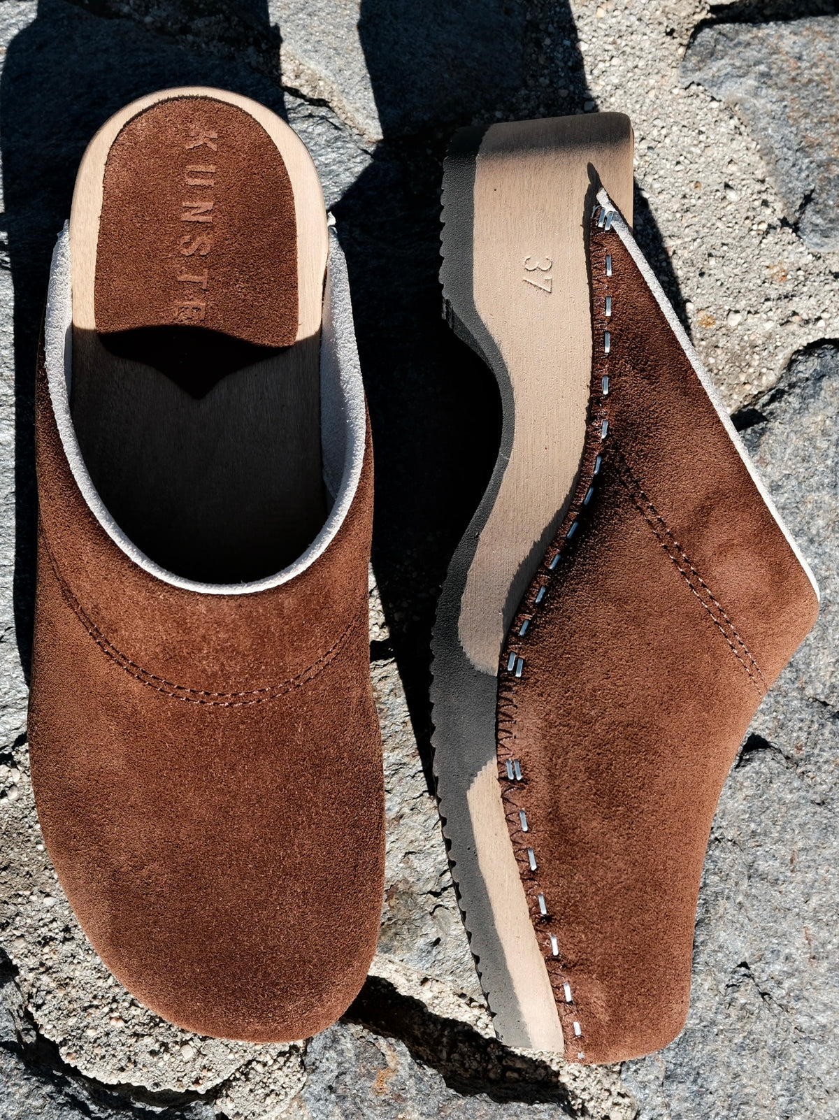 A pair of KUNSTEN suede clogs showing the bendable aspen wood sole, hand-hammered staples and rubber outsole