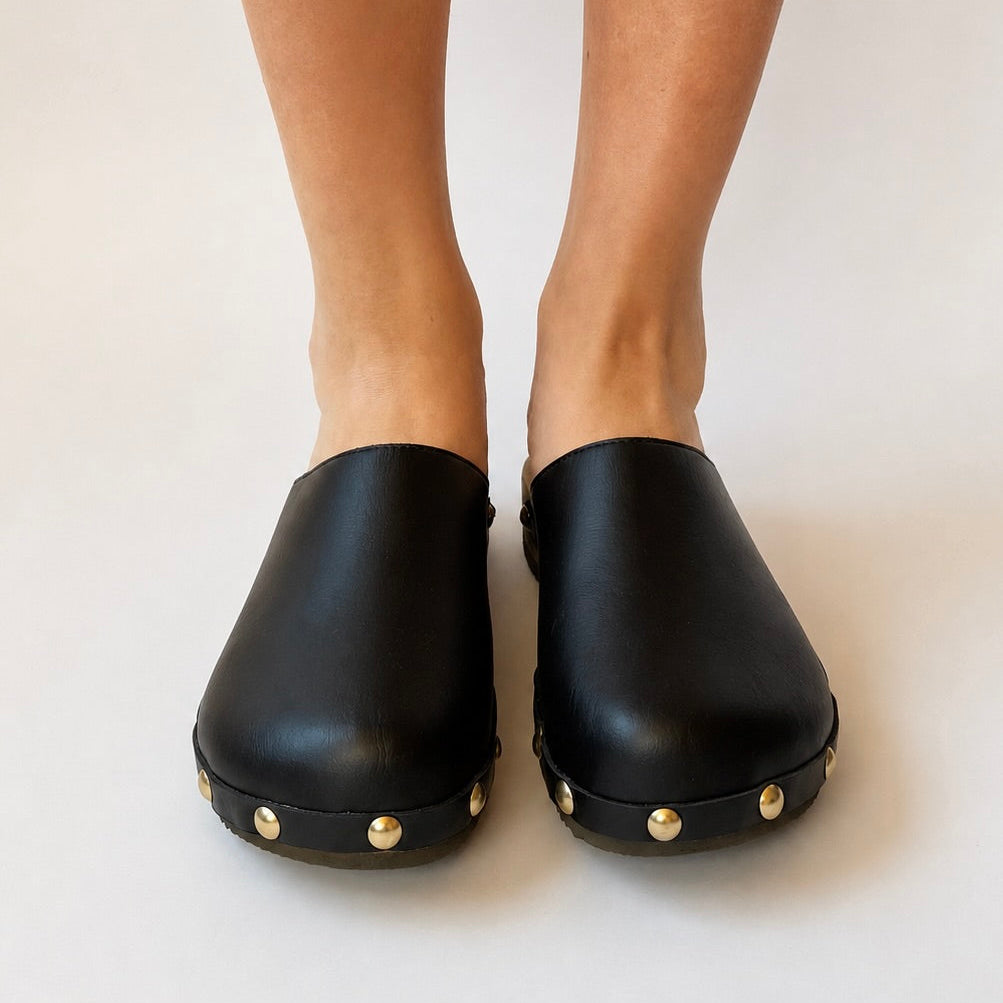 Black leather clogs with gold studs on a white background