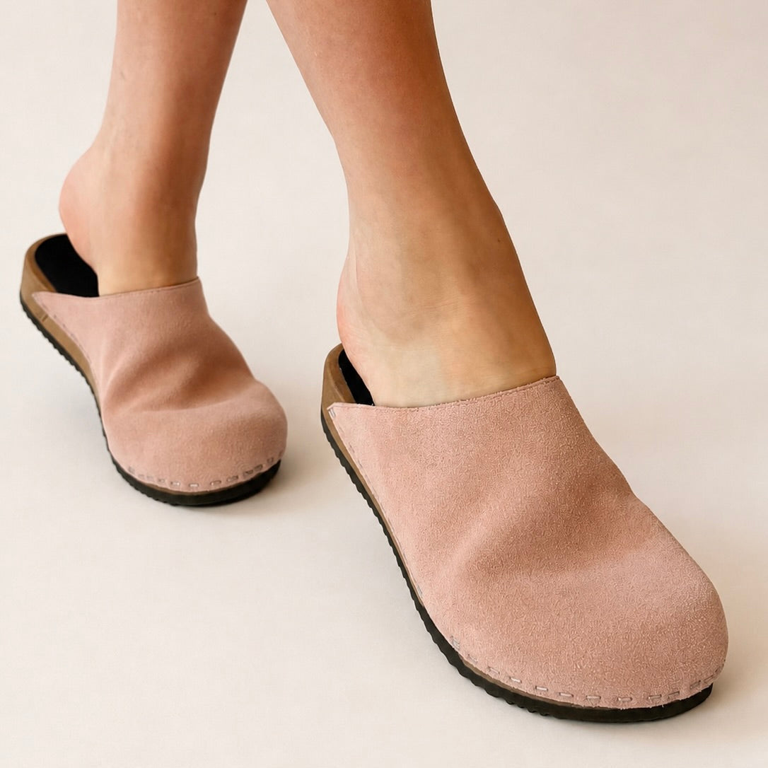 Pair of pink suede clogs on a white background