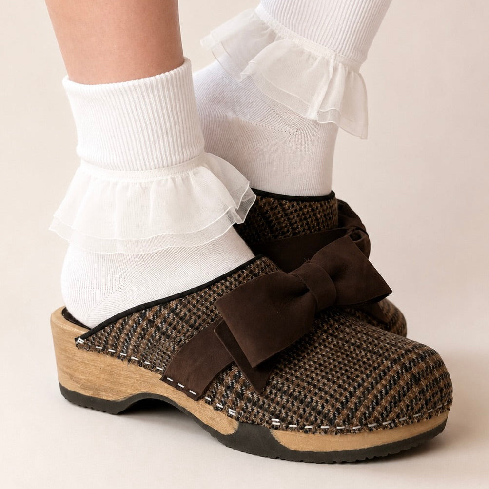 Pair of slippers with brown plaid pattern and large brown bows on a white background