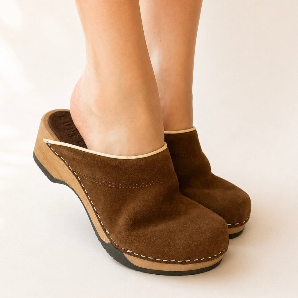 Pair of chocolate suede clogs on a white background