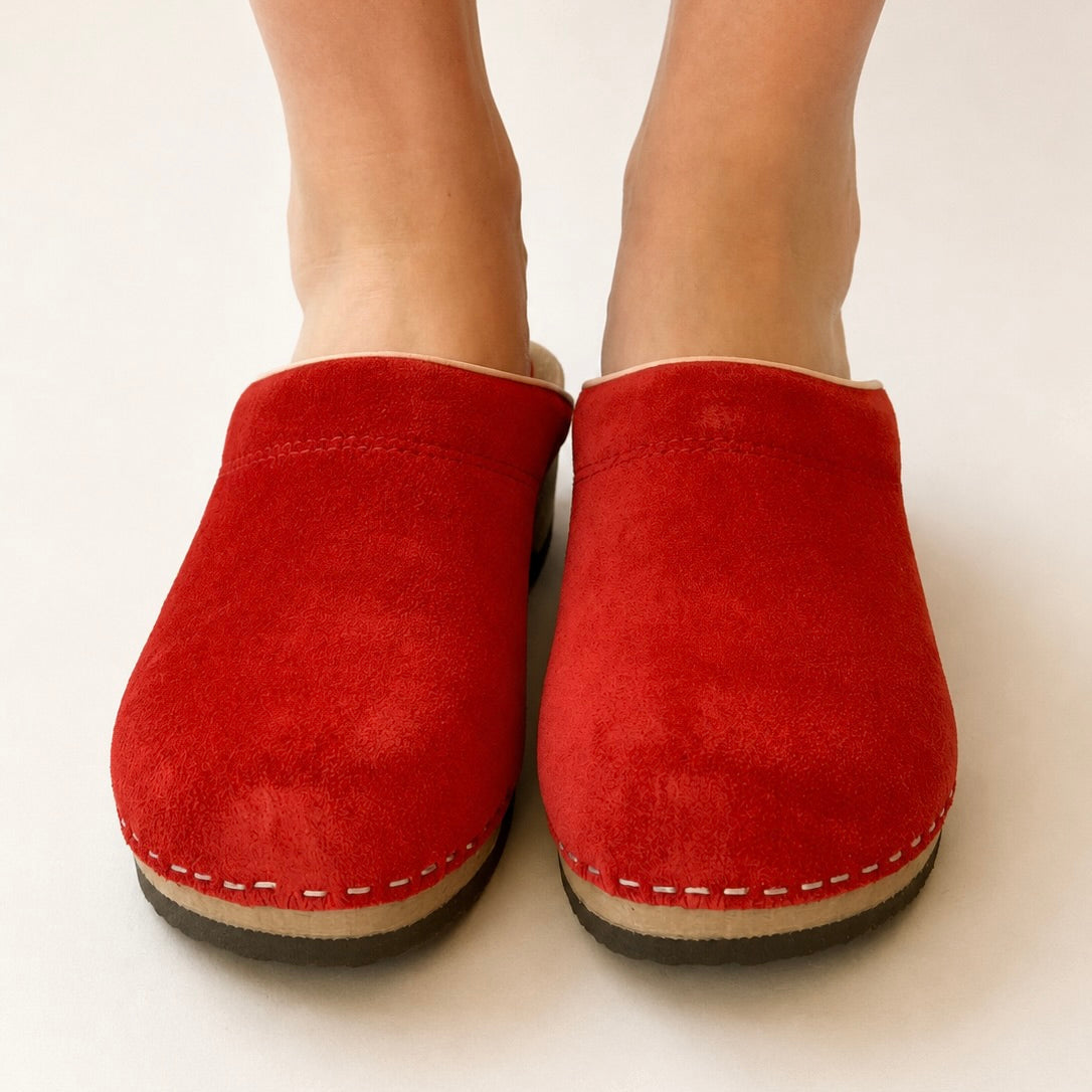Red clogs worn with blue jeans on a white background