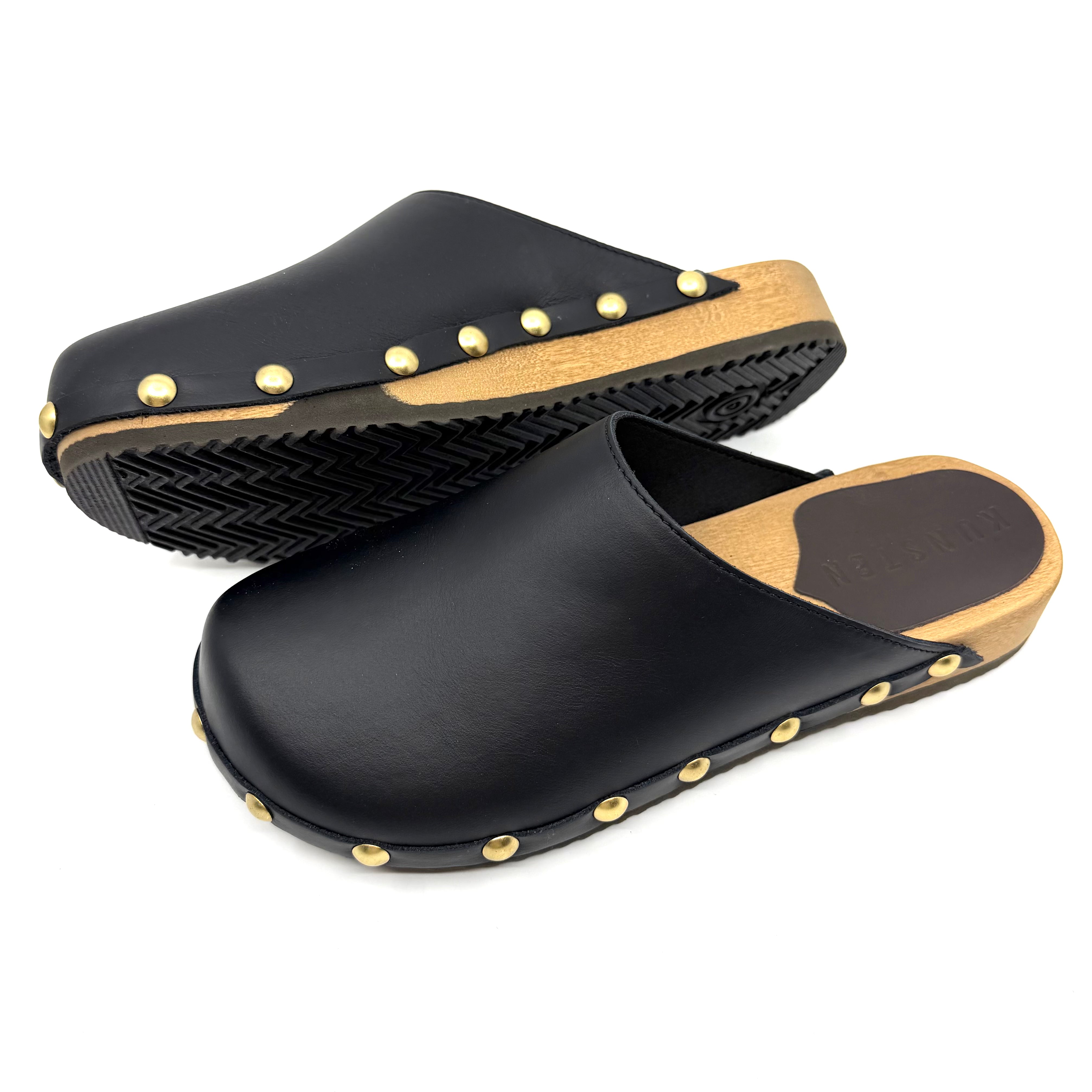 Black clogs with gold studs and wooden soles on a white background