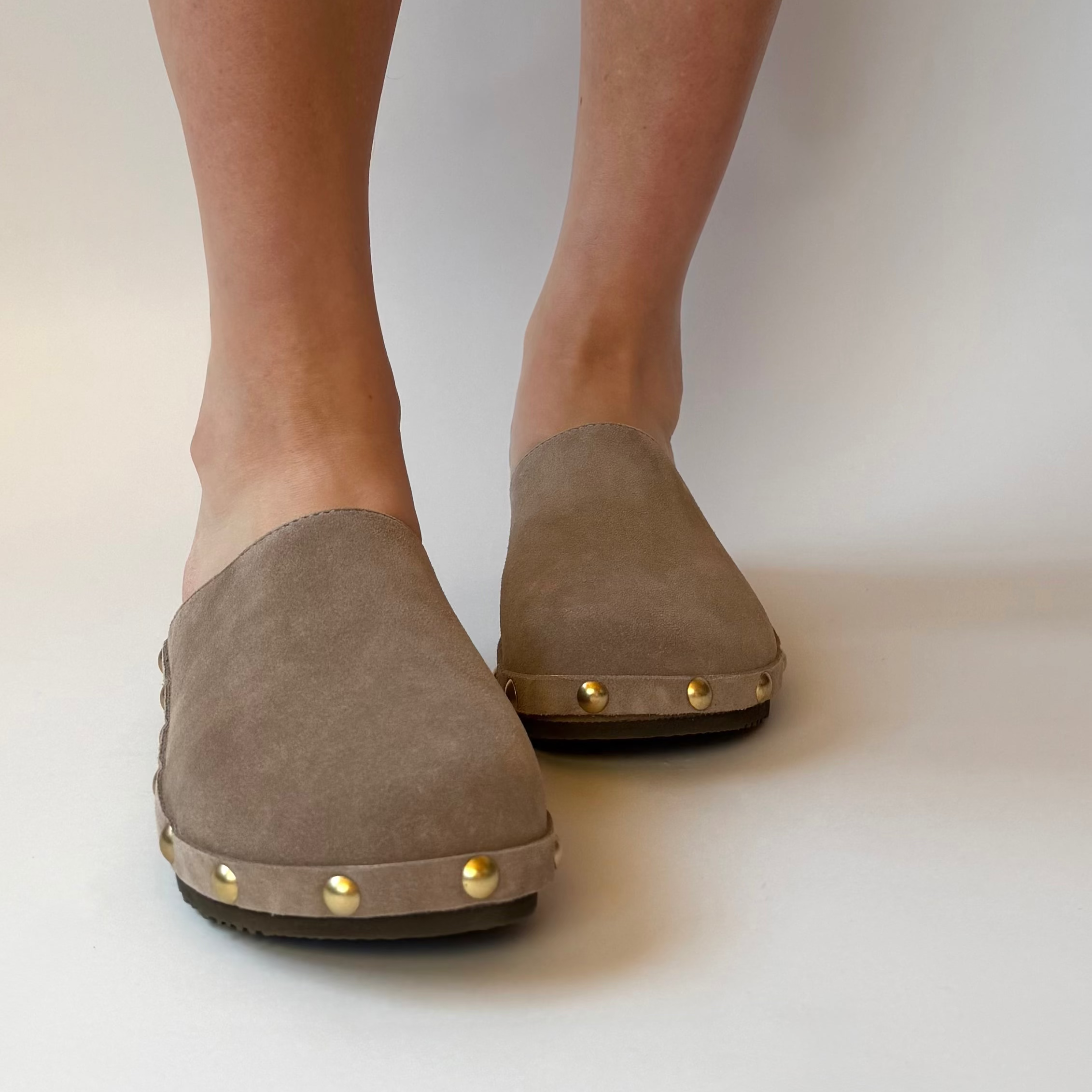 Brown loafers with gold studs worn by a person on a white background