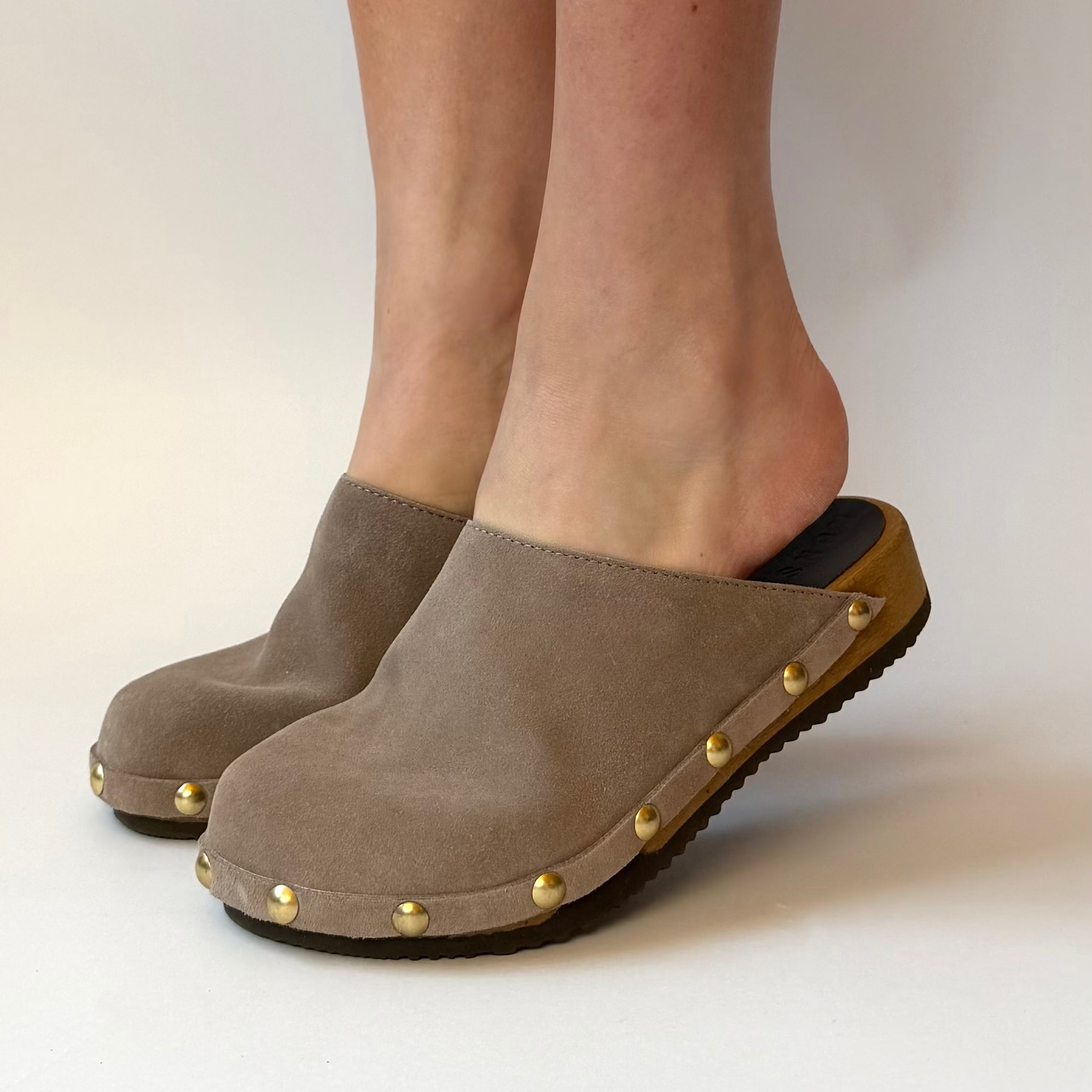 Brown clogs with gold studs worn by a person on a plain background