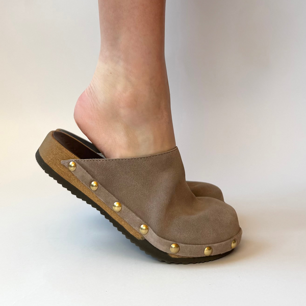 Brown clog shoe with gold studs worn by a person on a light background