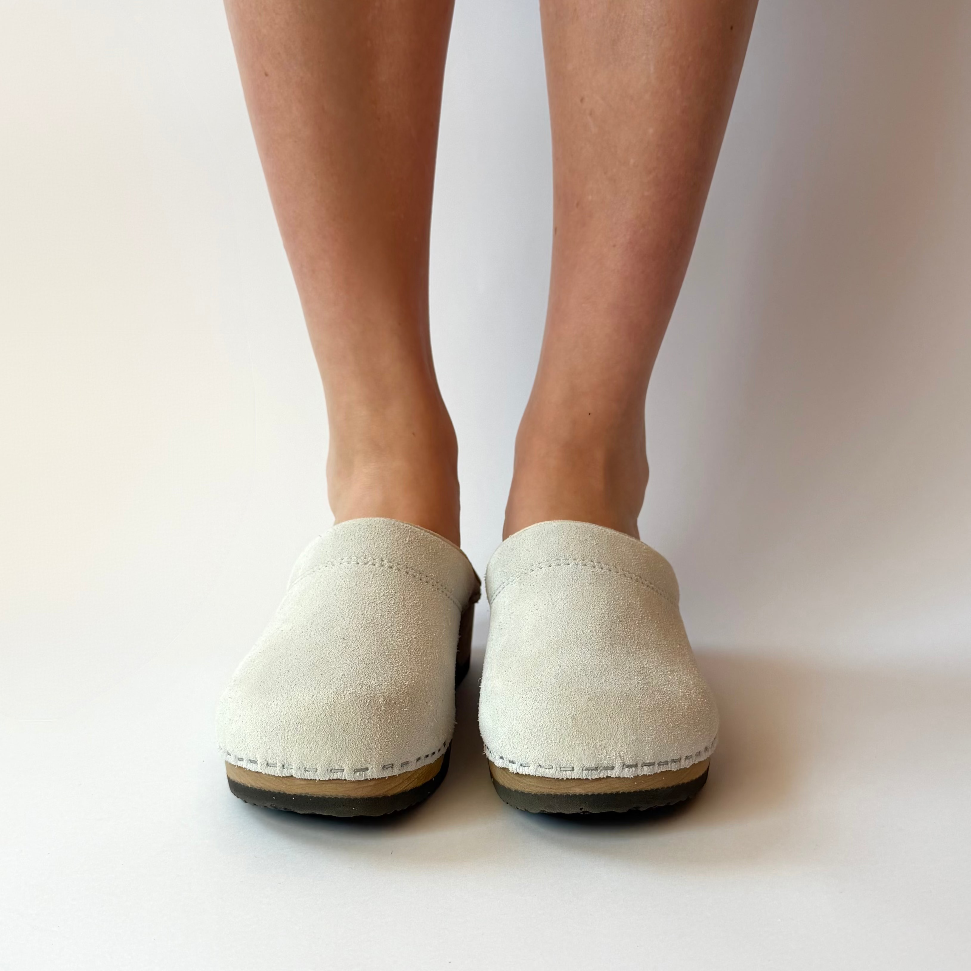 White slip-on shoes worn by a person on a plain background