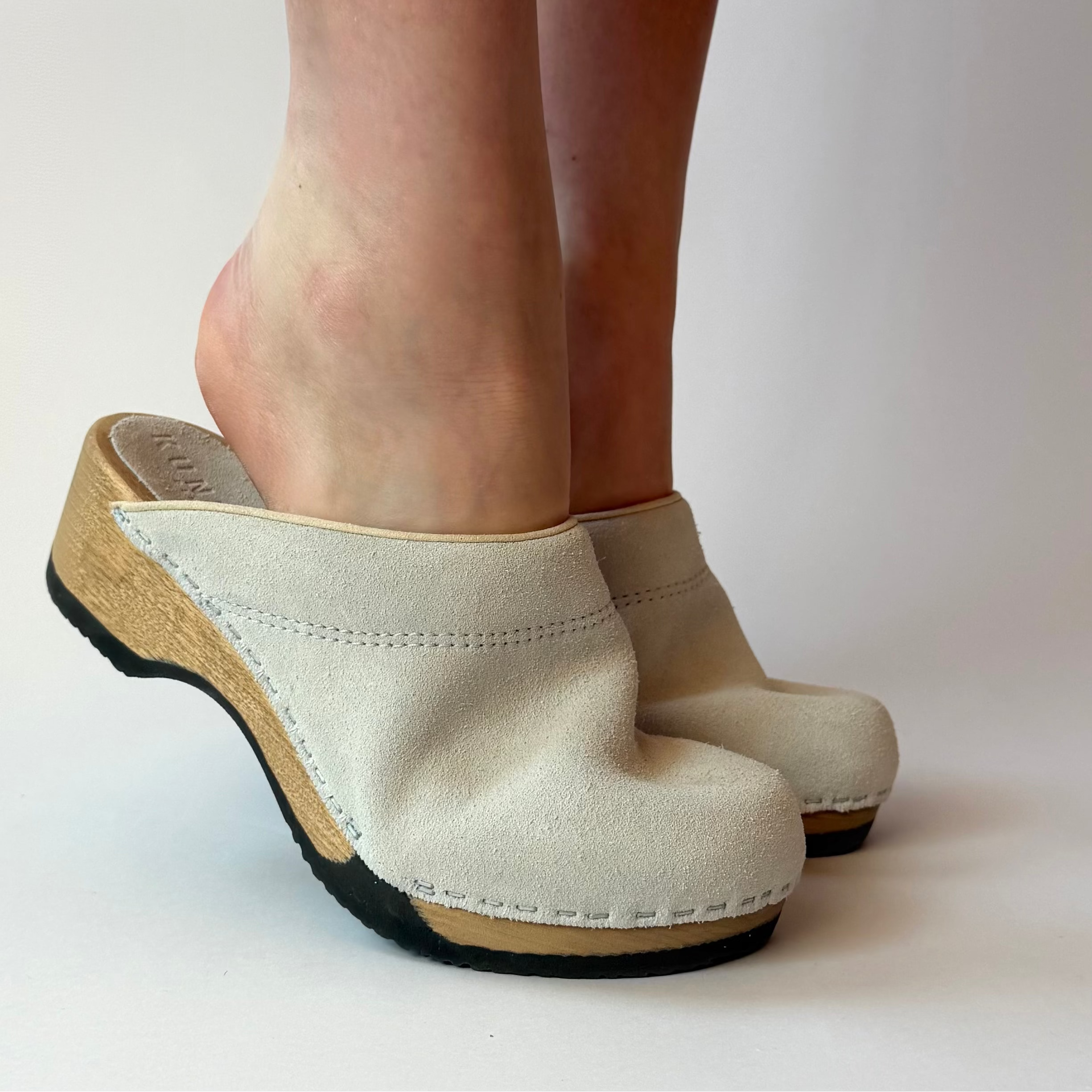 Beige clogs worn by a person on a plain background