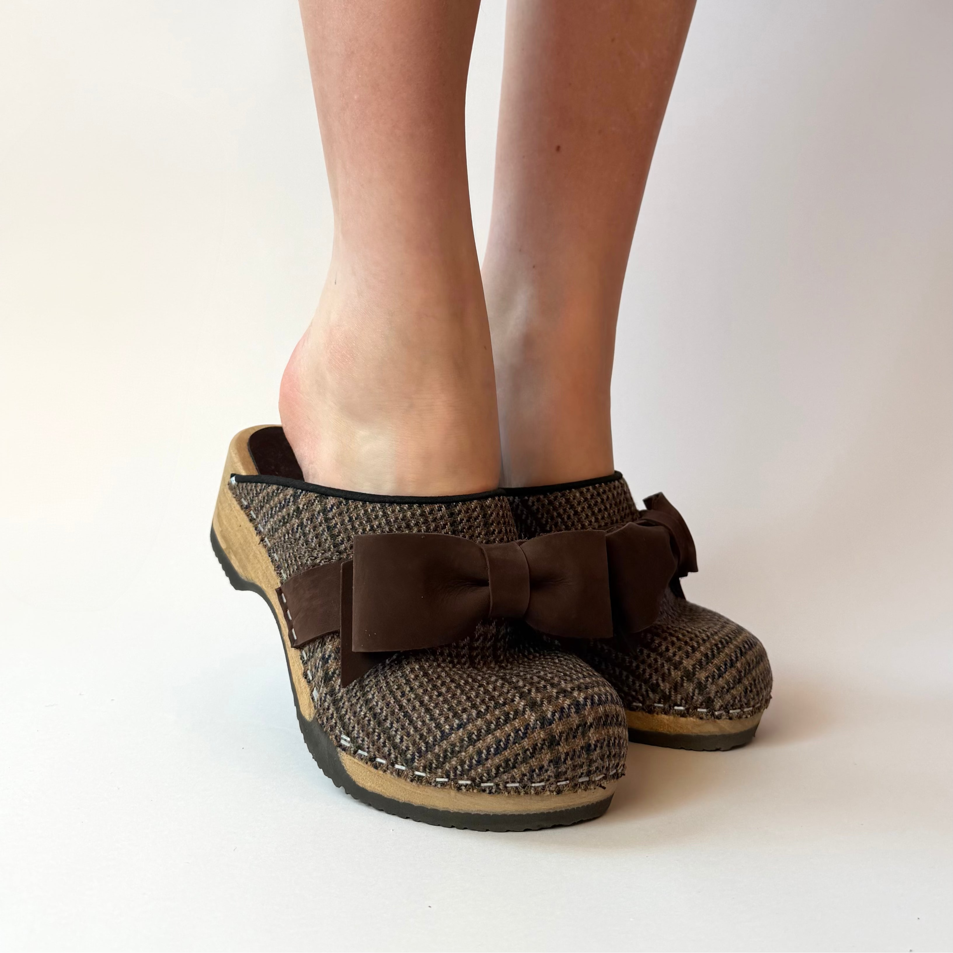 Brown houndstooth patterned clogs with a bow on a white background