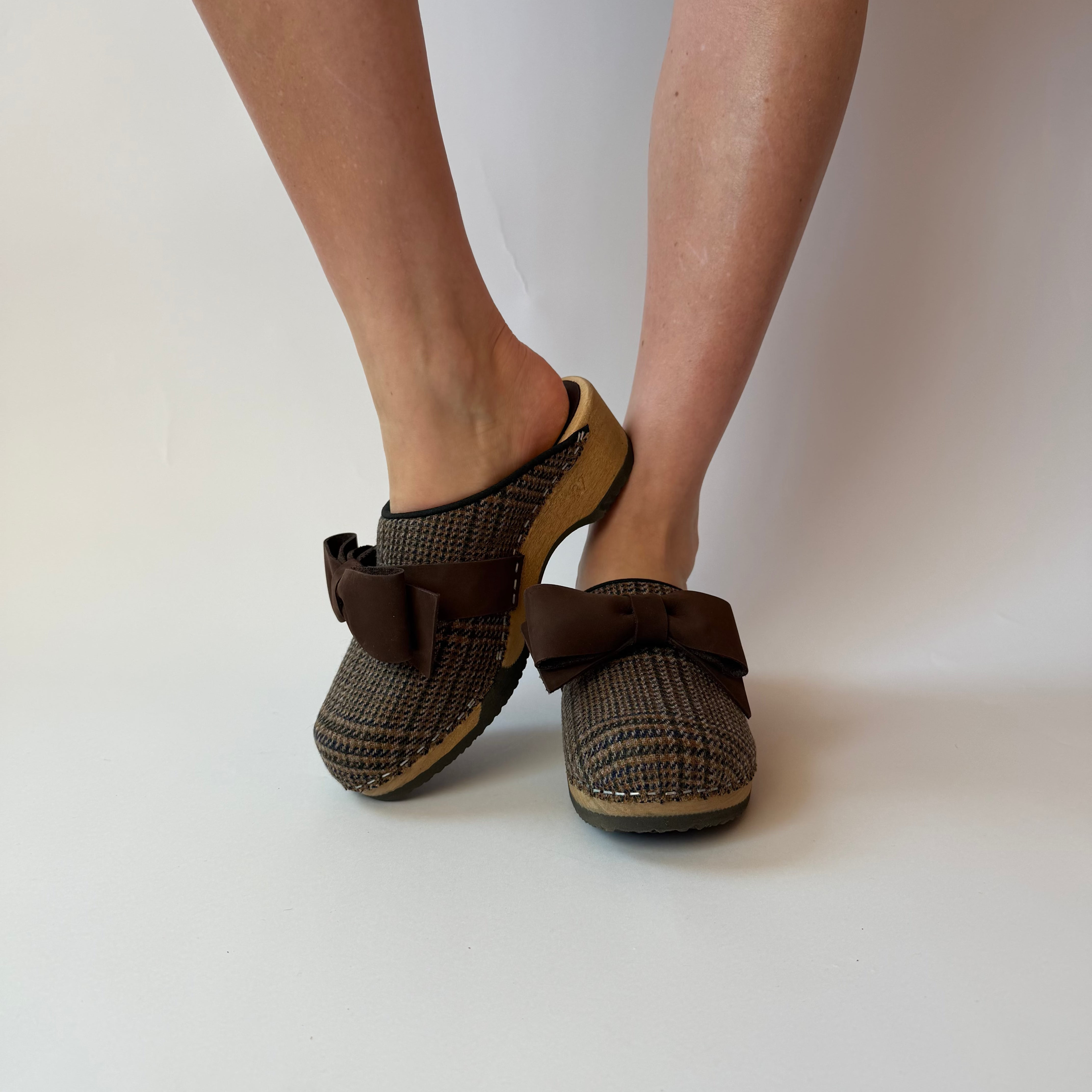 Brown checkered clogs worn by a person on a white background