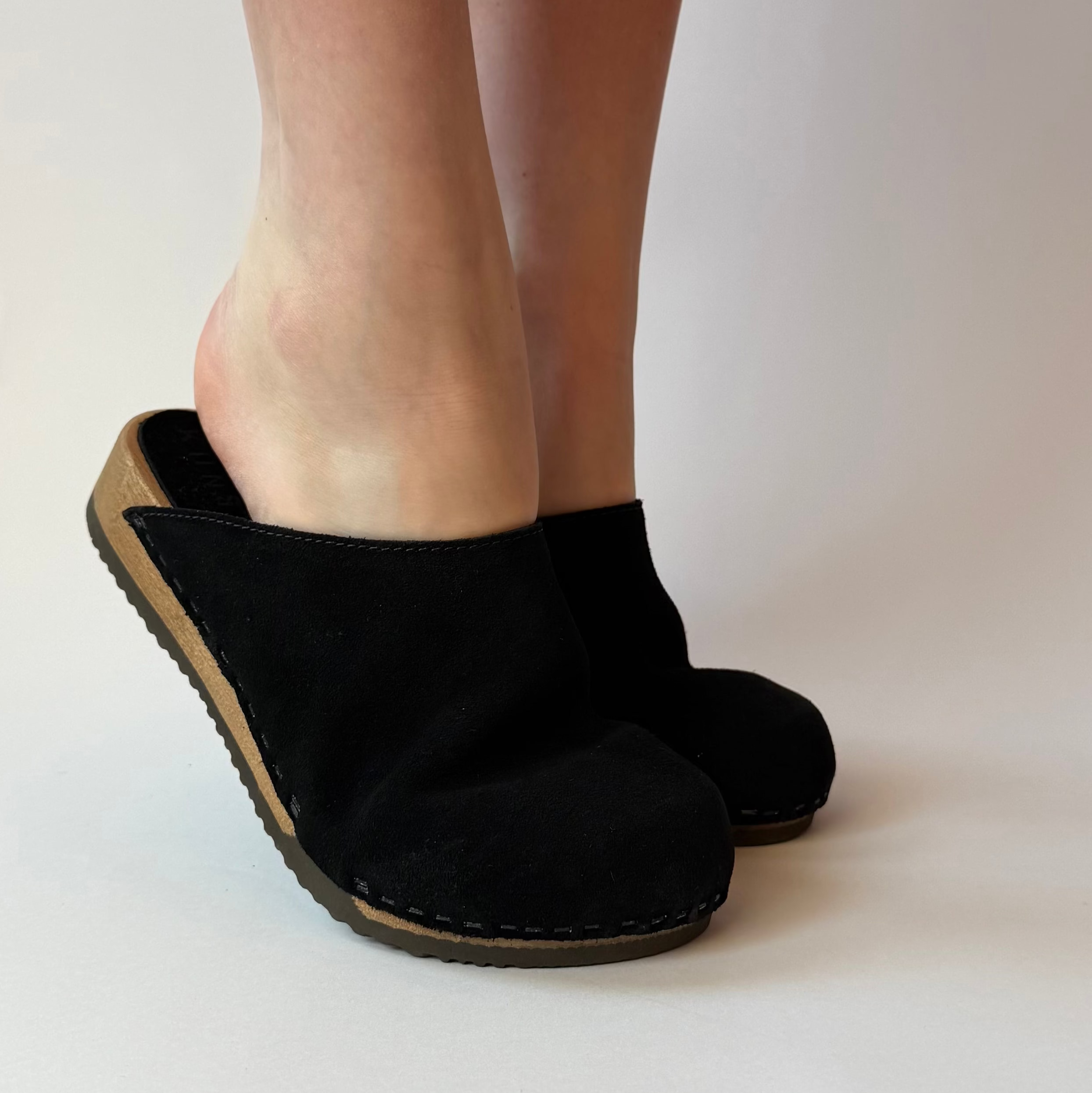 Black slip-on shoes worn by a person on a plain background