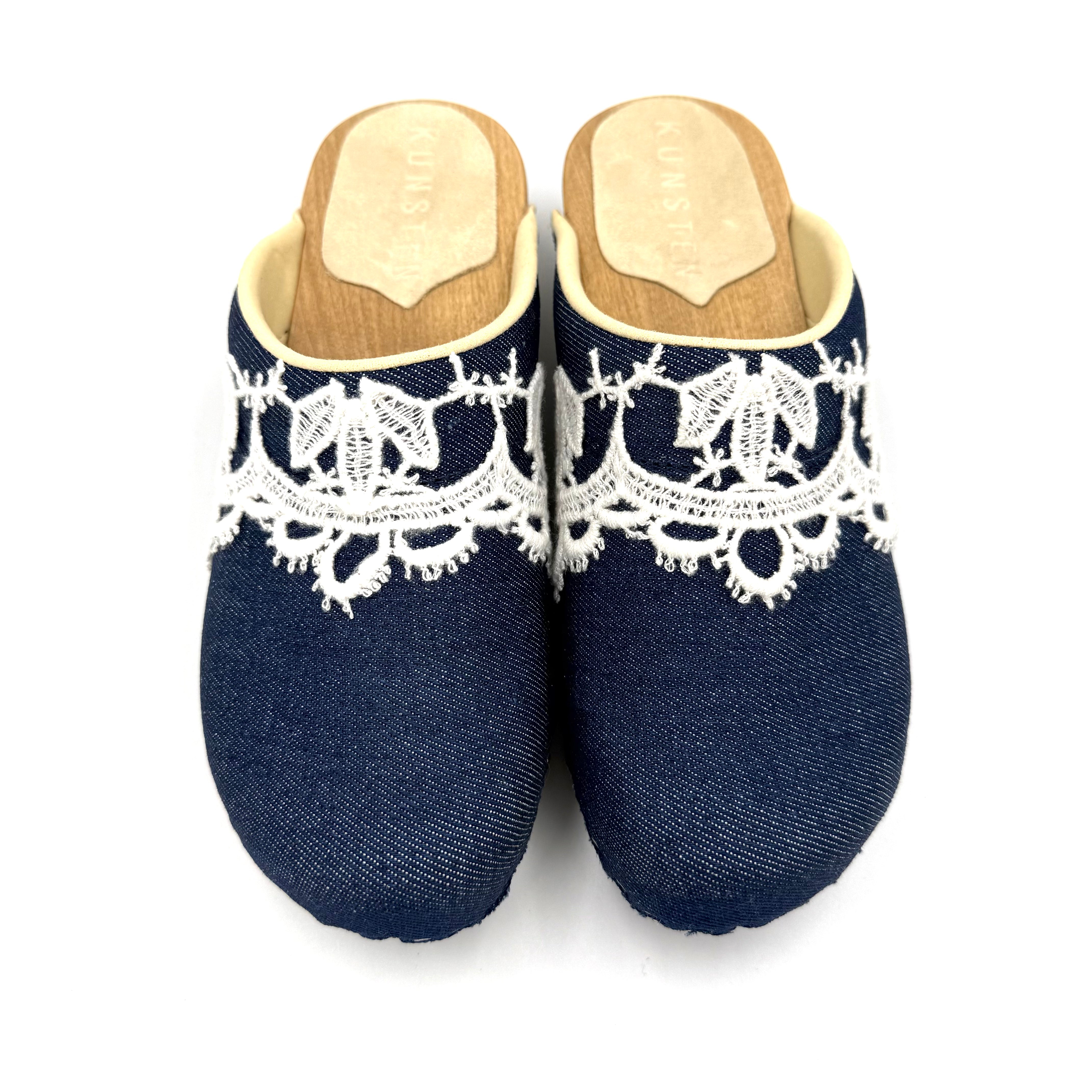 Pair of navy blue slippers with white lace details on a white background