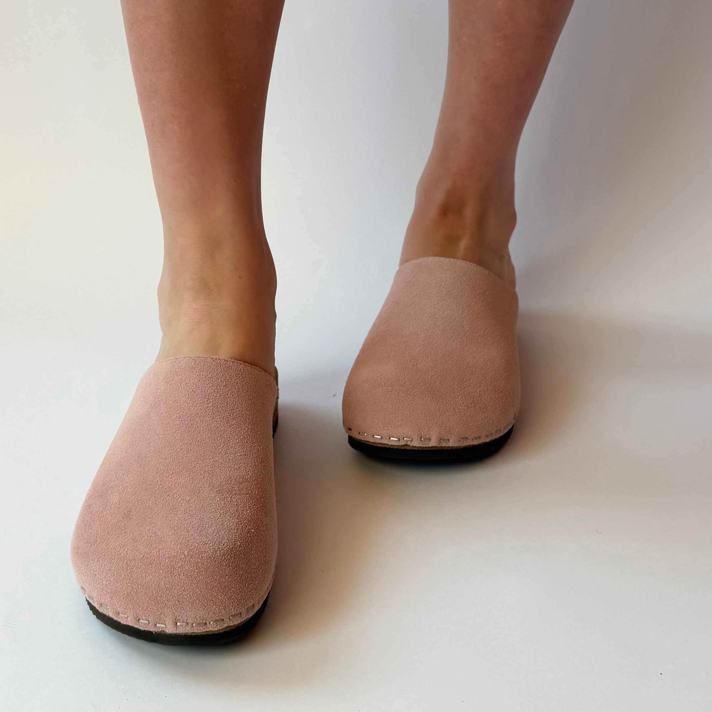 Pair of pink suede shoes worn by a person on a white background