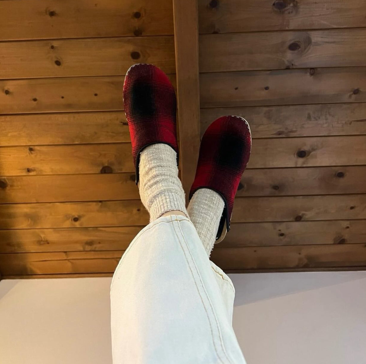 Red slippers on feet with white socks against a wooden floor background