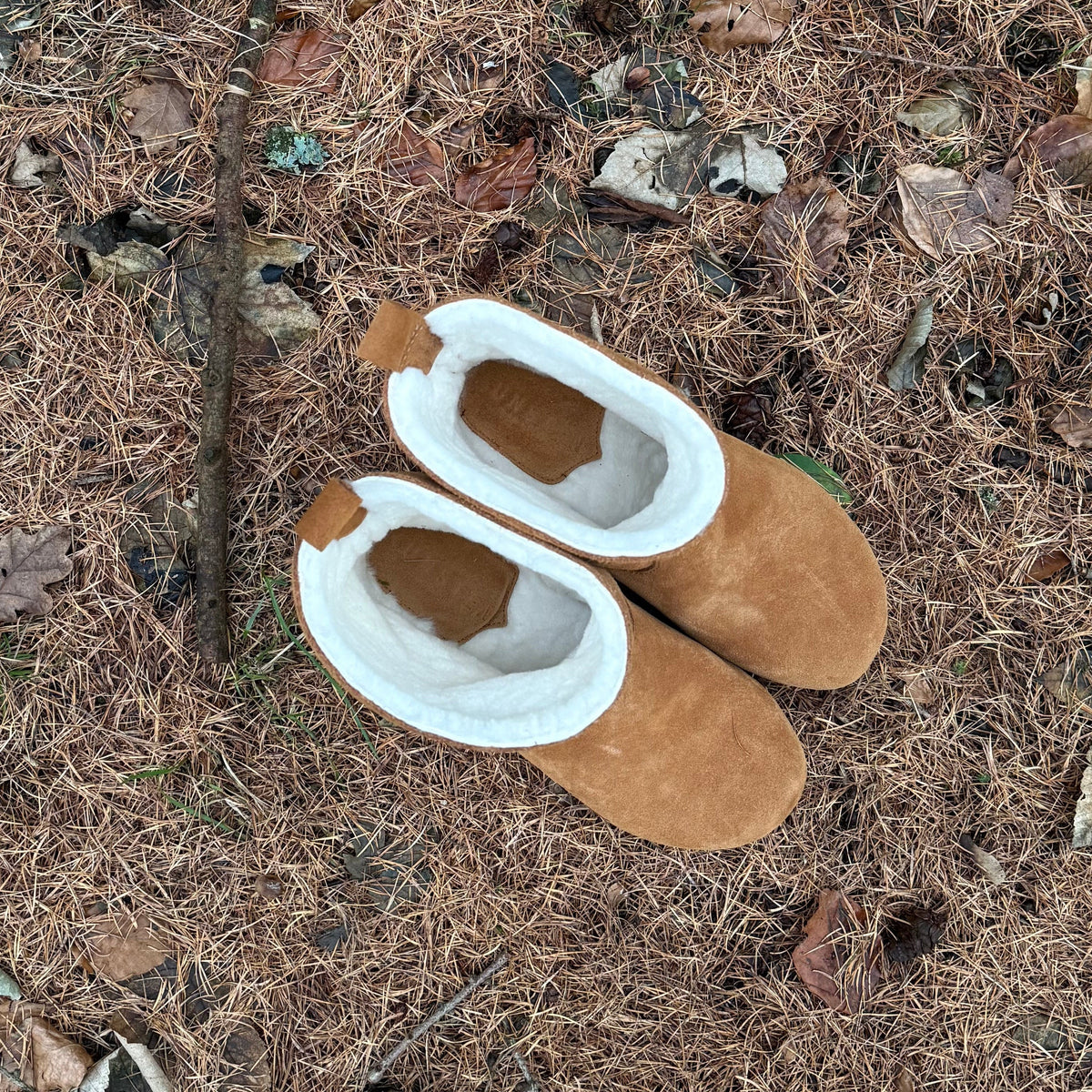 Pair of brown slippers with white soles on a textured ground surface