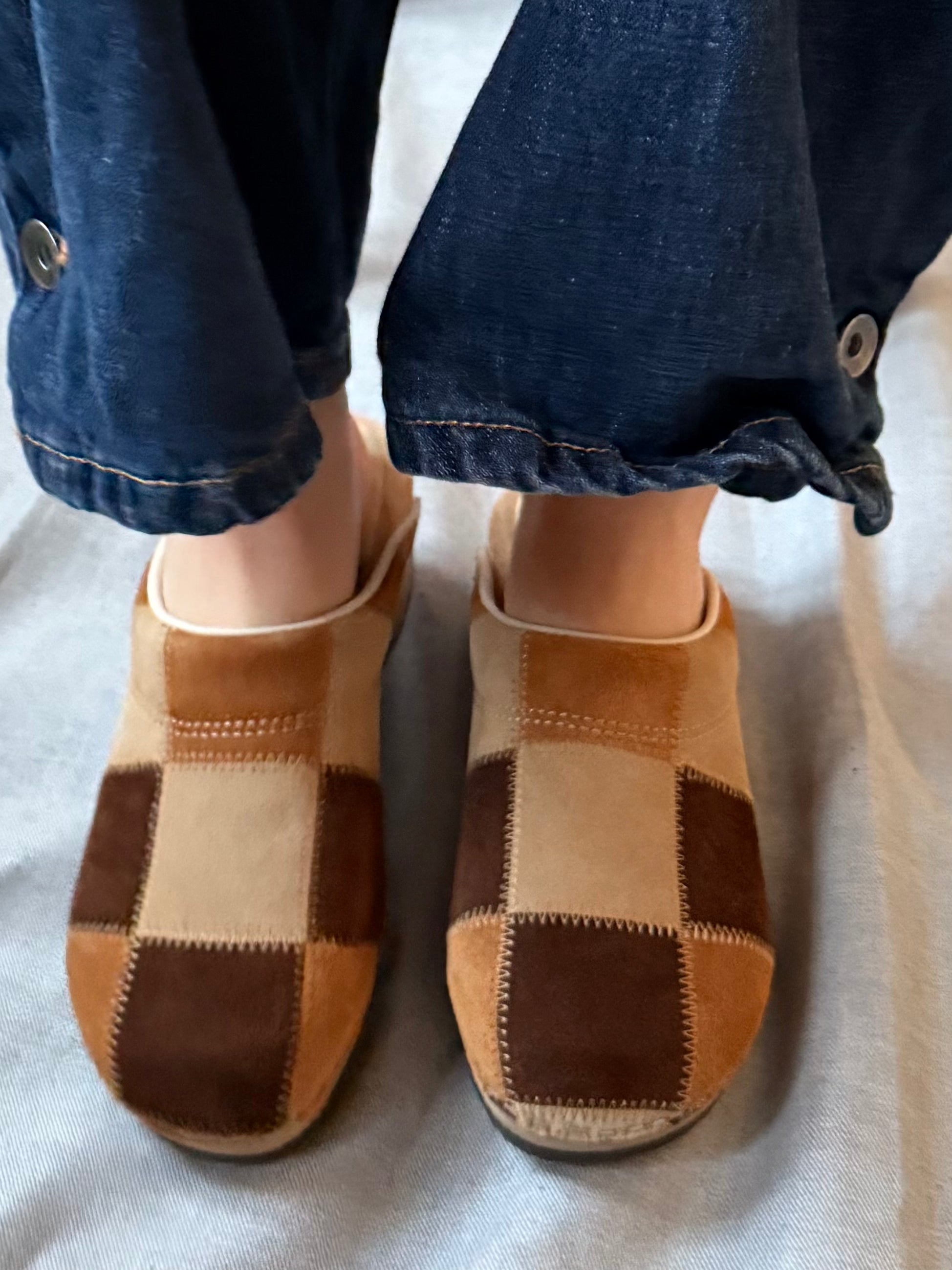 Pair of checkered slippers worn with rolled-up jeans on a light background