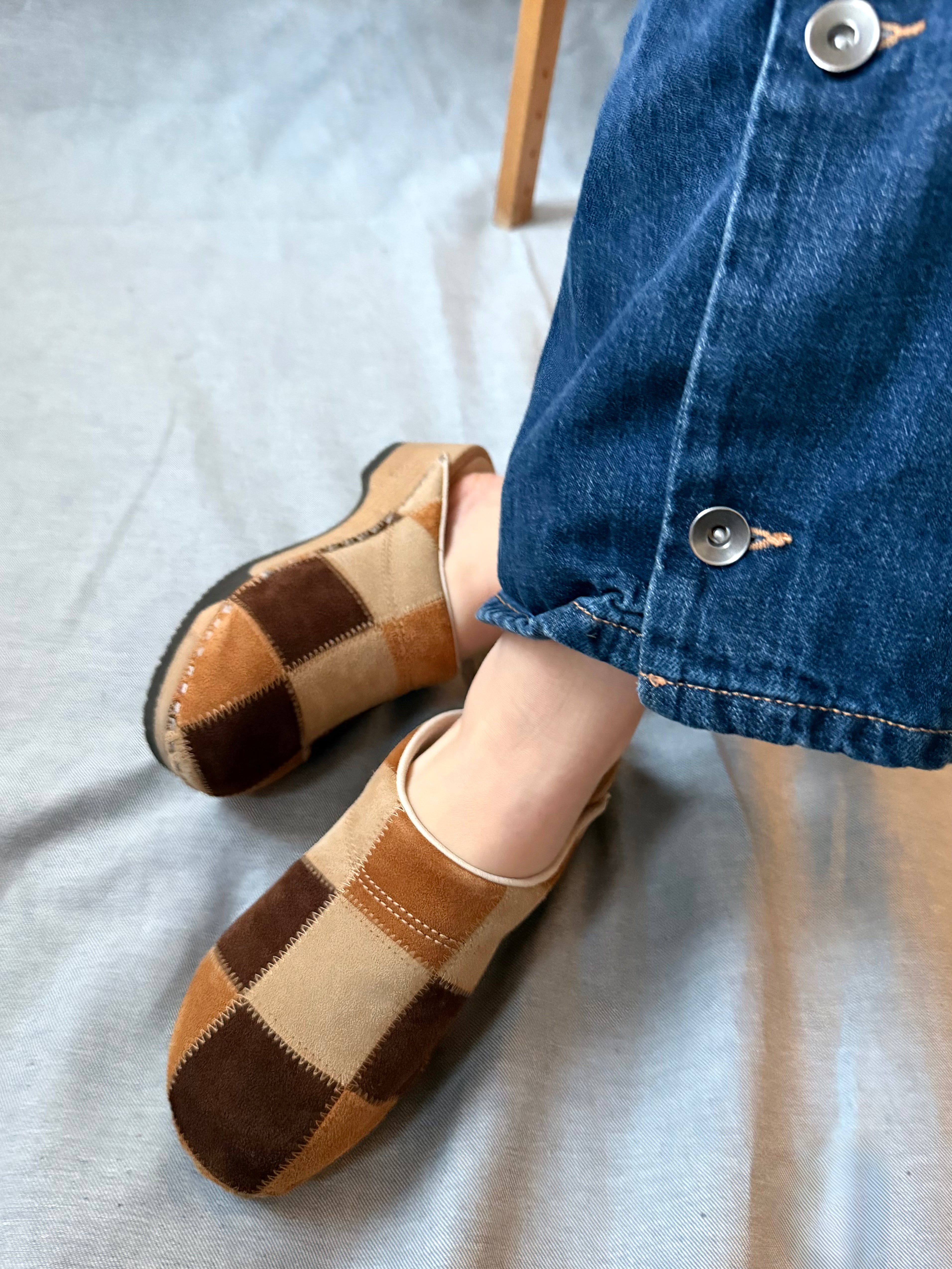 Pair of checkered slippers worn with a denim jacket on a light gray background