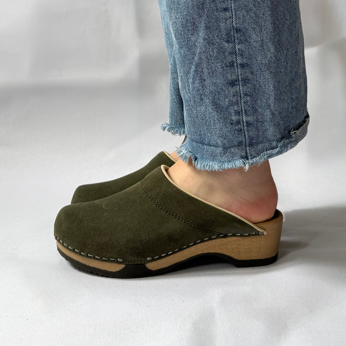 Person wearing green suede clogs with a white background