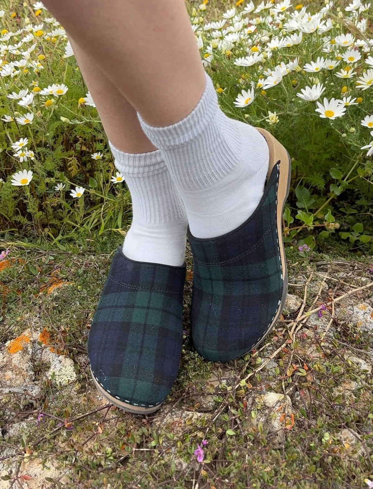 Plaid slippers worn with white socks on a natural background with flowers.