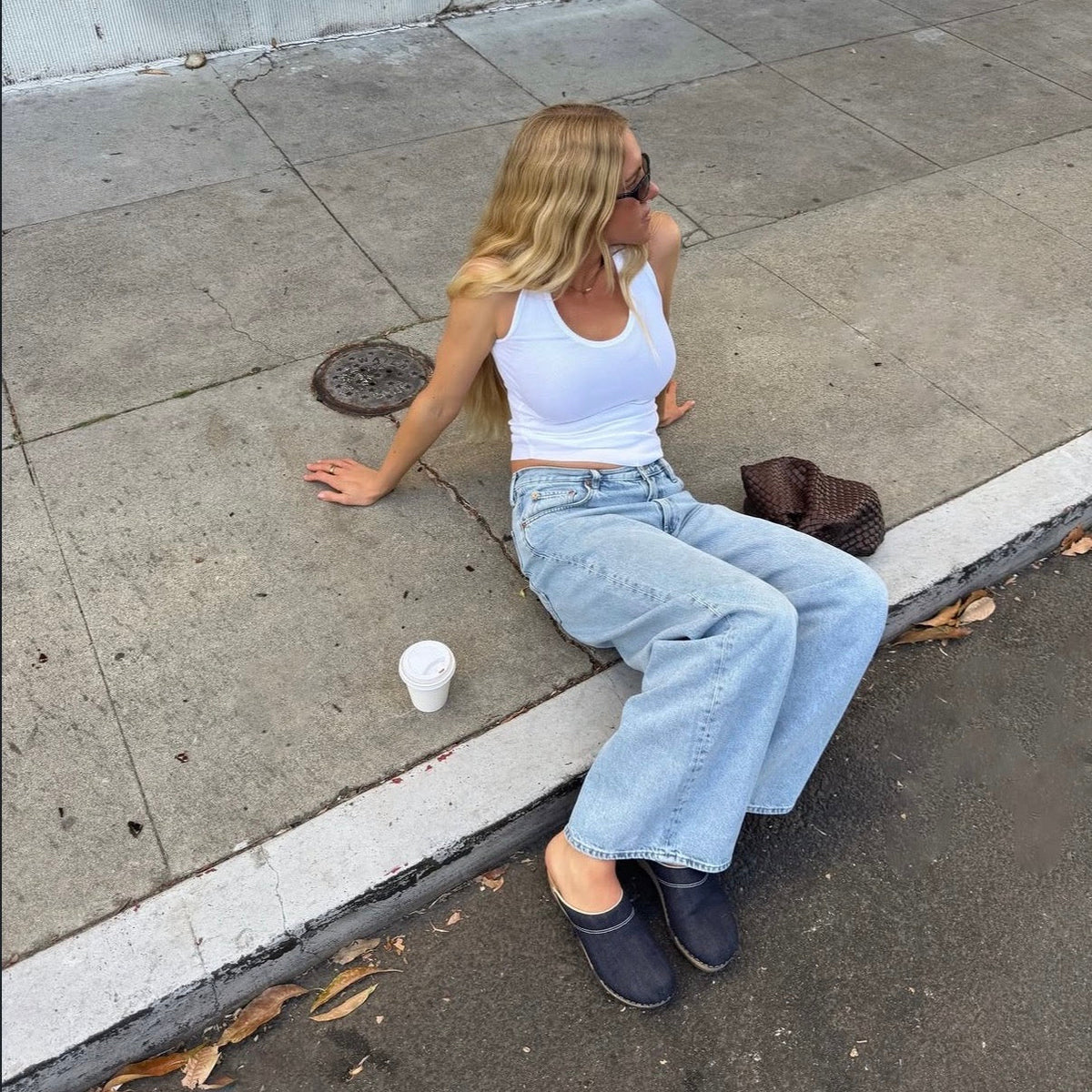 Woman sitting on a curb wearing KUNSTEN clogs