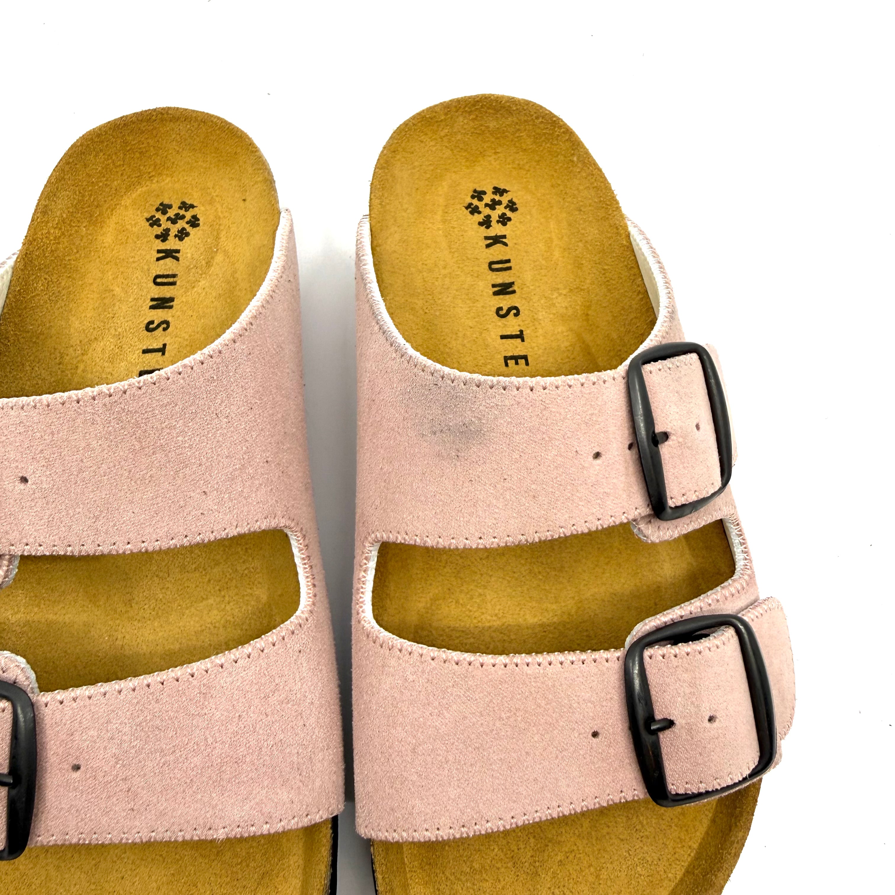 Pair of beige sandals with black buckles on a white background