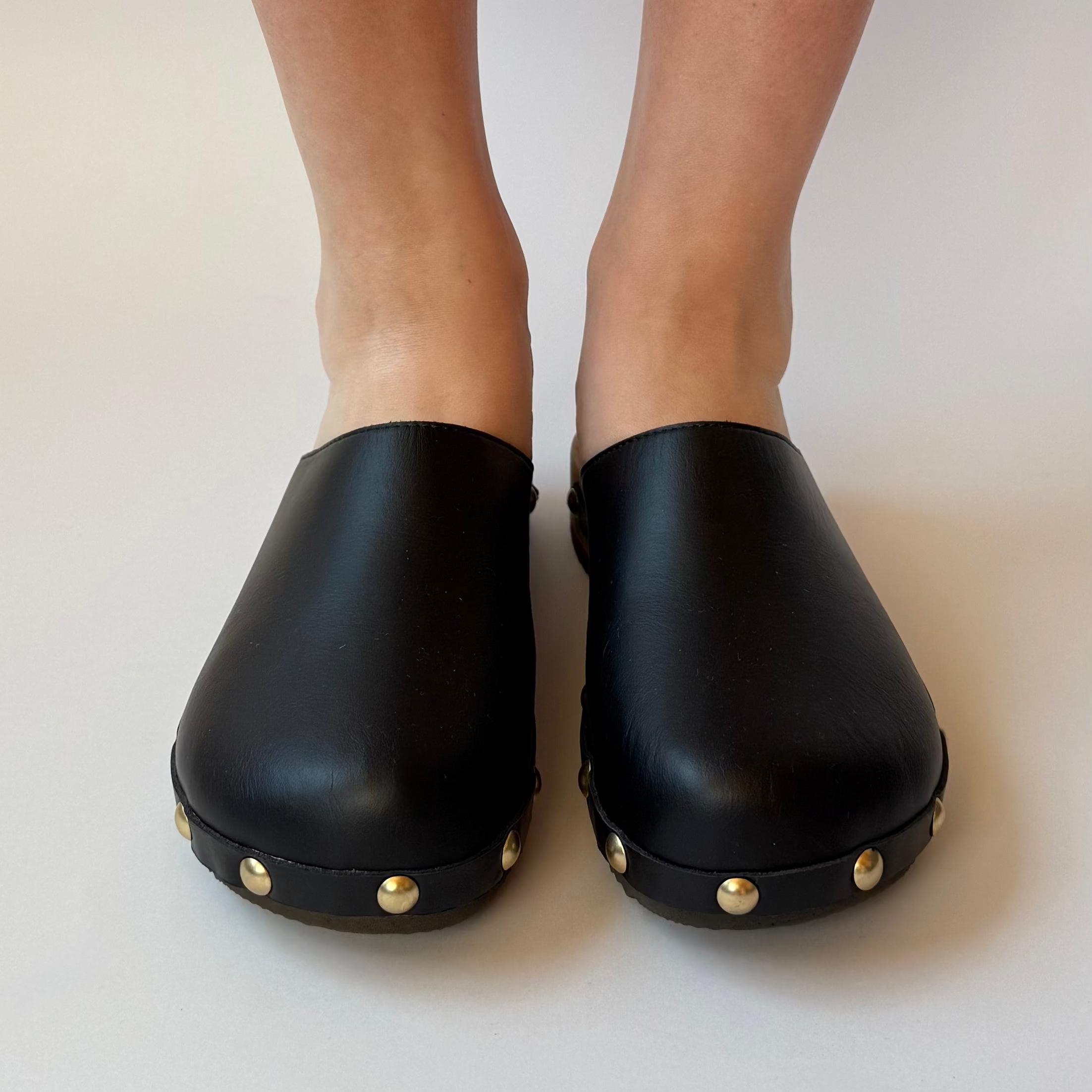 Black clogs with gold studs on a white background