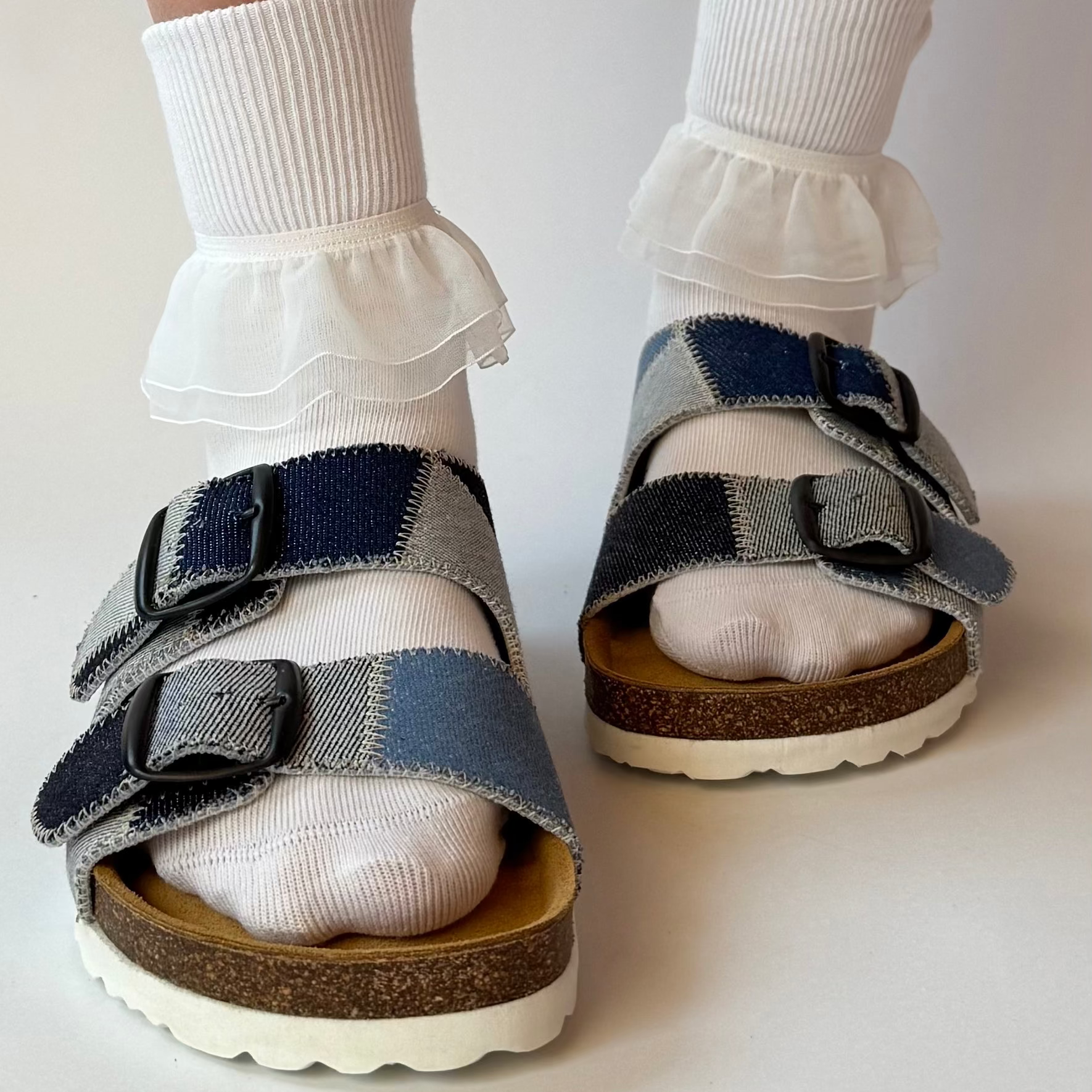 Children's sandals with ruffled socks on a plain background