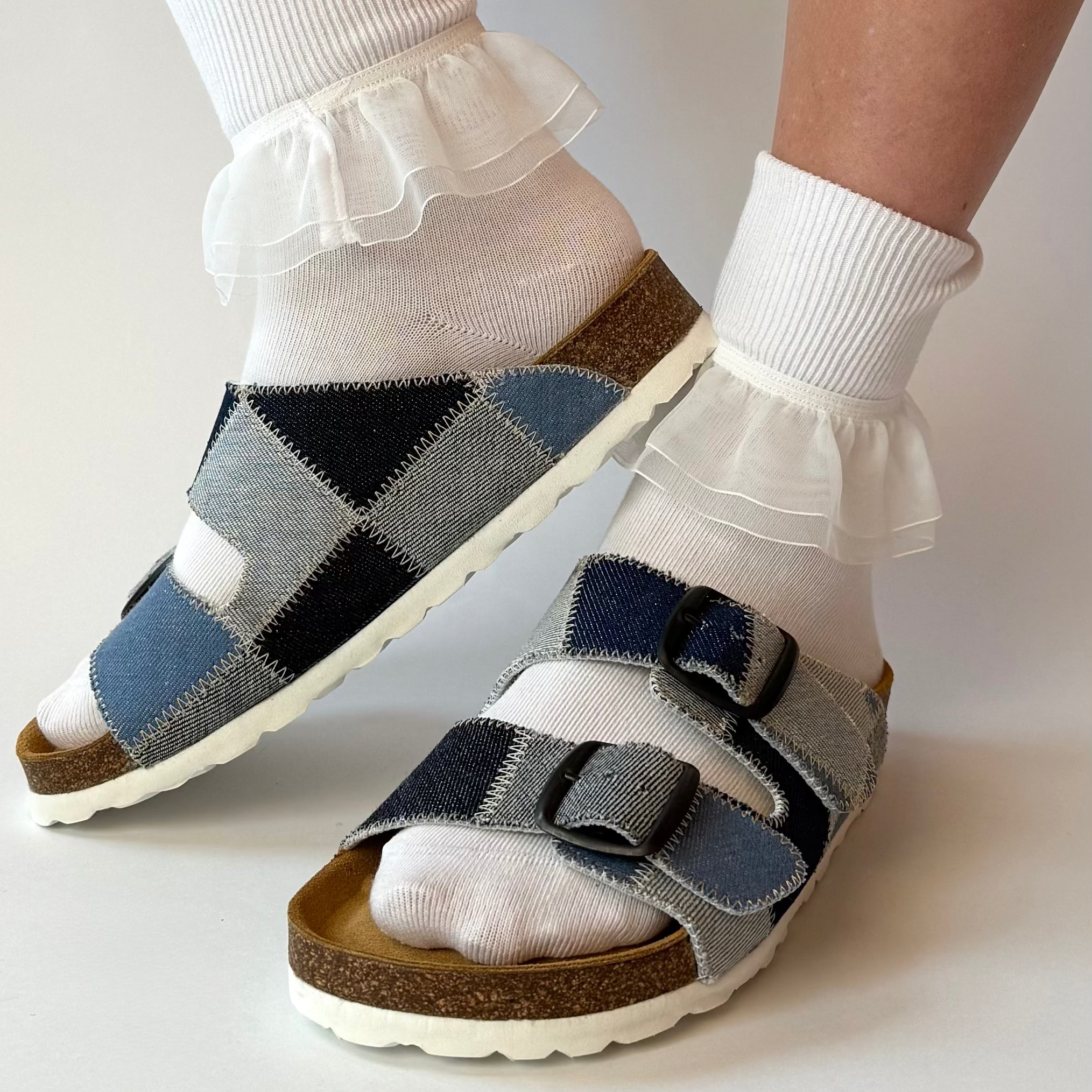 Pair of sandals with a geometric pattern worn with white socks on a plain background