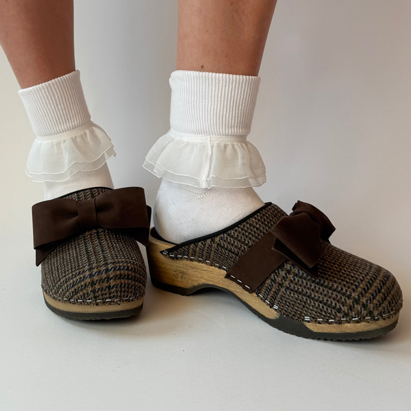 Brown woven clogs with a bow on white socks against a plain background