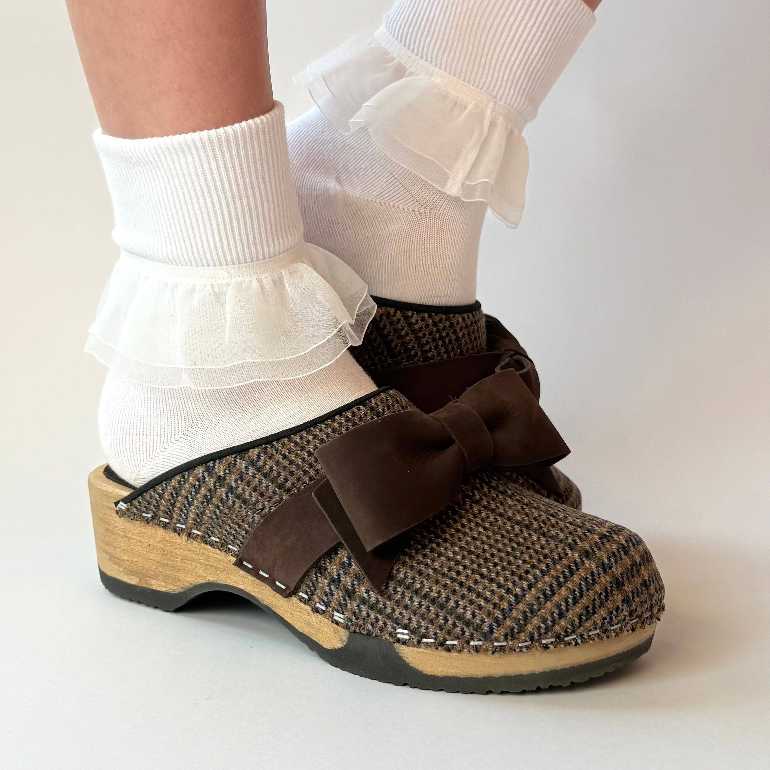 Brown clogs with decorative bows worn with white socks on a light background