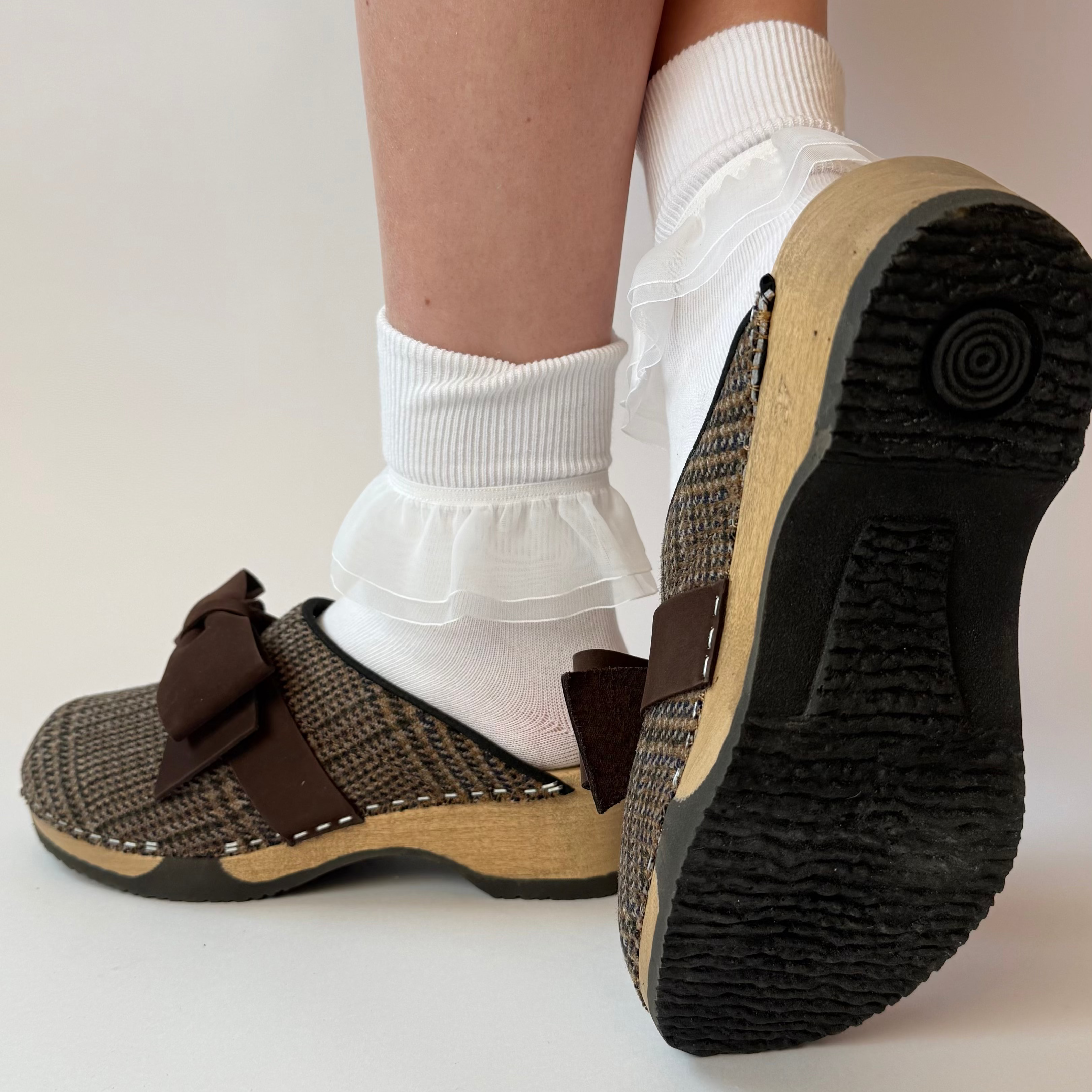 Brown clogs with wooden soles worn with white socks on a light background