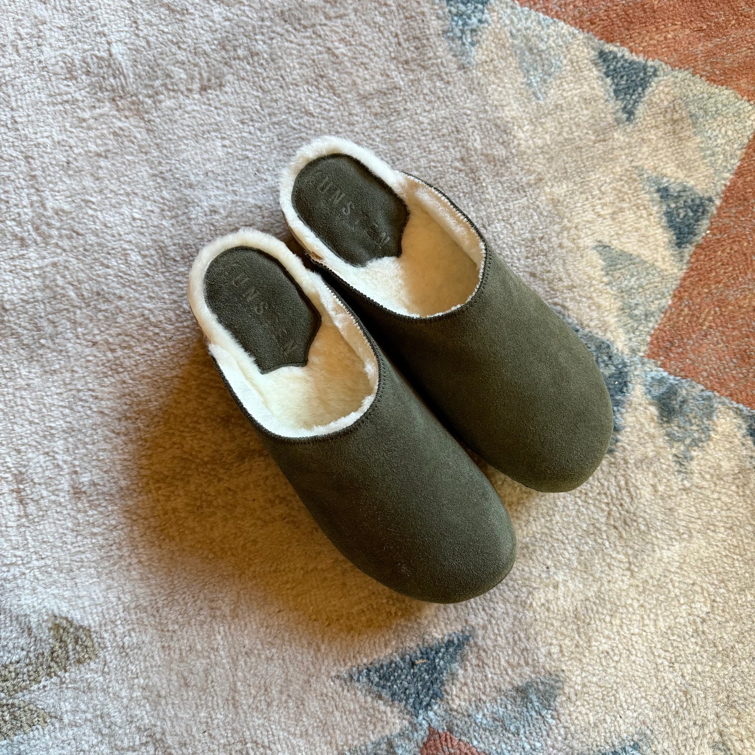 Pair of green slippers with white lining on a textured surface