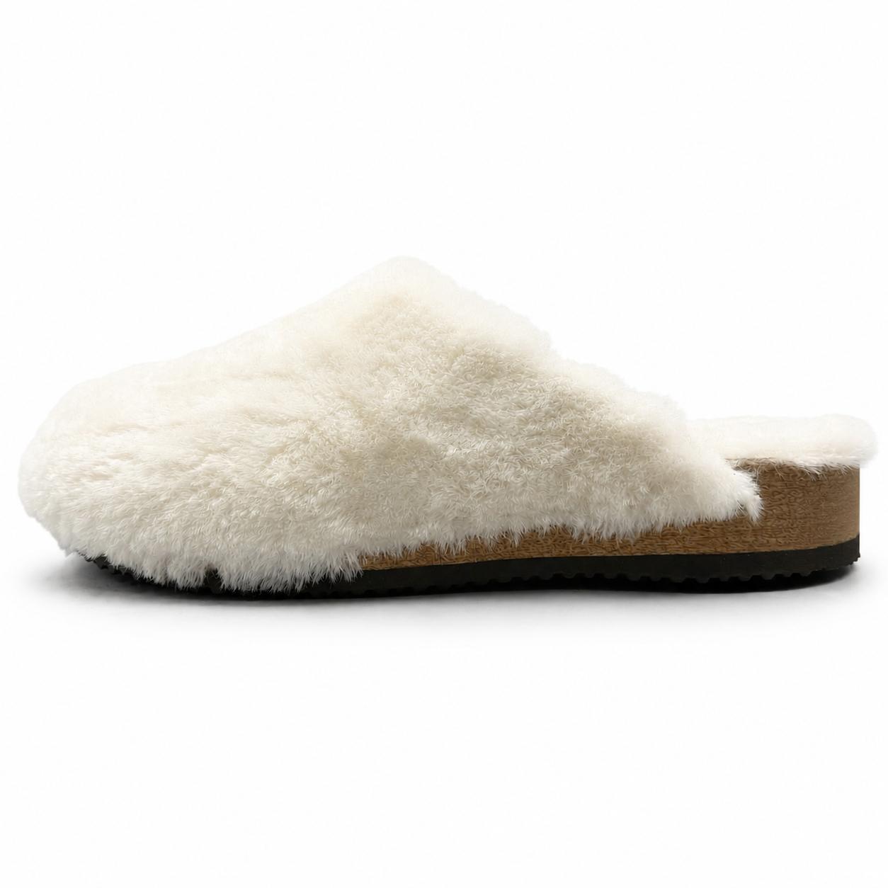 A close-up of a person wearing blue jeans and light blue knit socks with white faux-fur trim, standing on a light gray studio floor. One shoe is lifted to show the black treaded sole and tan footbed.