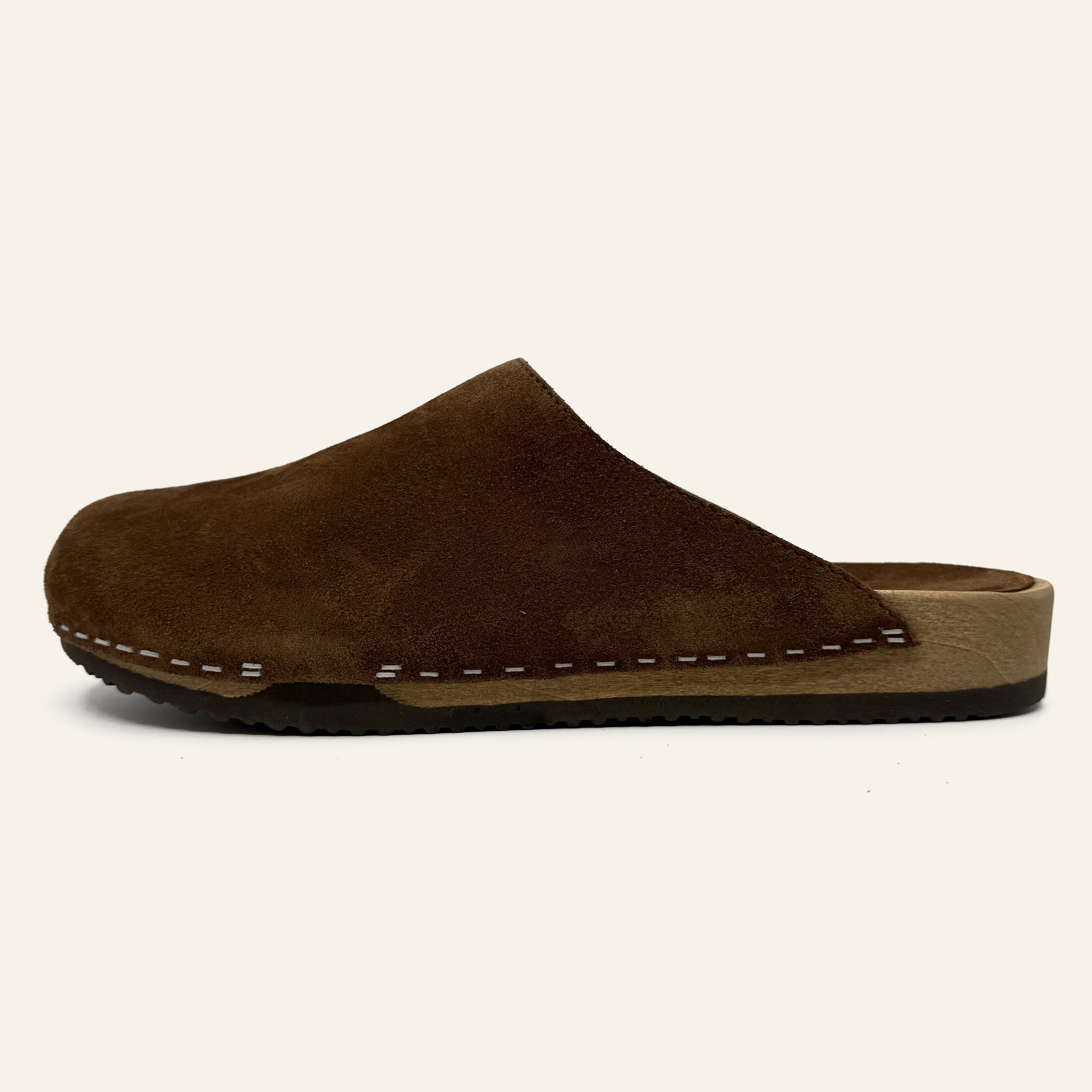 A dark brown suede clog with white contrast stitching along the side, a tan footbed, and a black outsole, shown against a solid off-white background.
