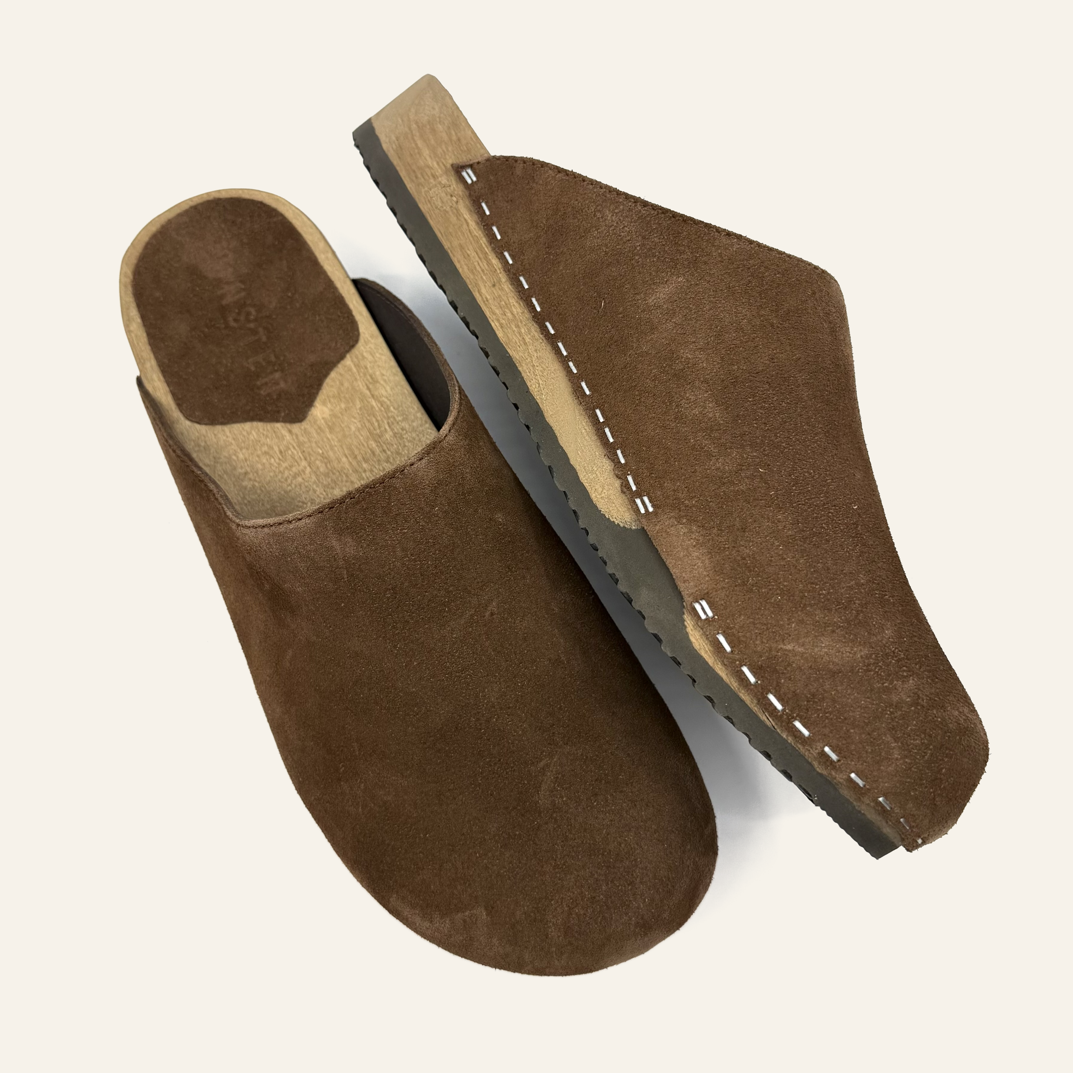A pair of brown suede clogs with white contrast stitching and a light tan insole, shown from top and side angles on a light cream background.