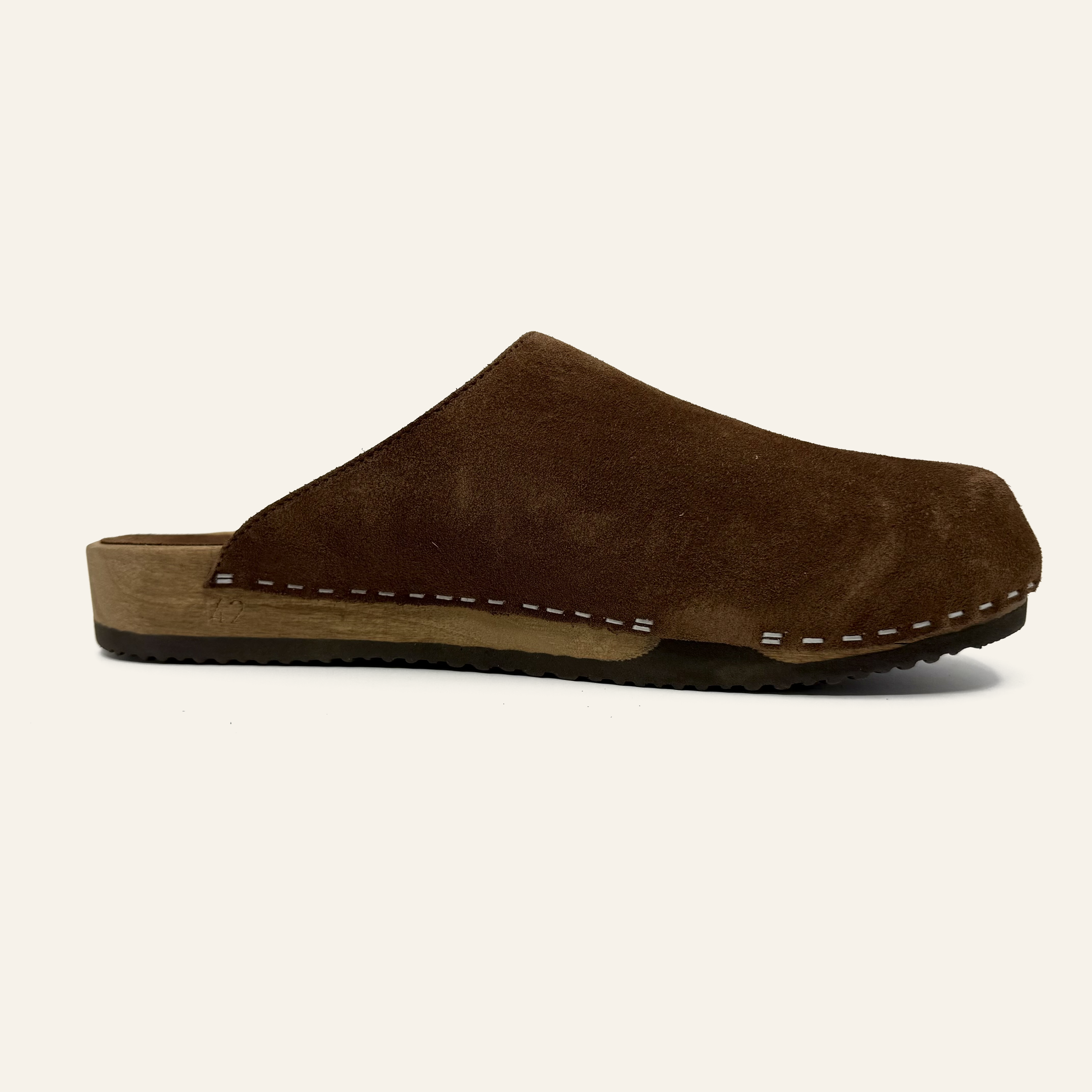A single dark brown suede clog with white contrast stitching and a tan cork-like midsole, shown in profile against a light cream background.