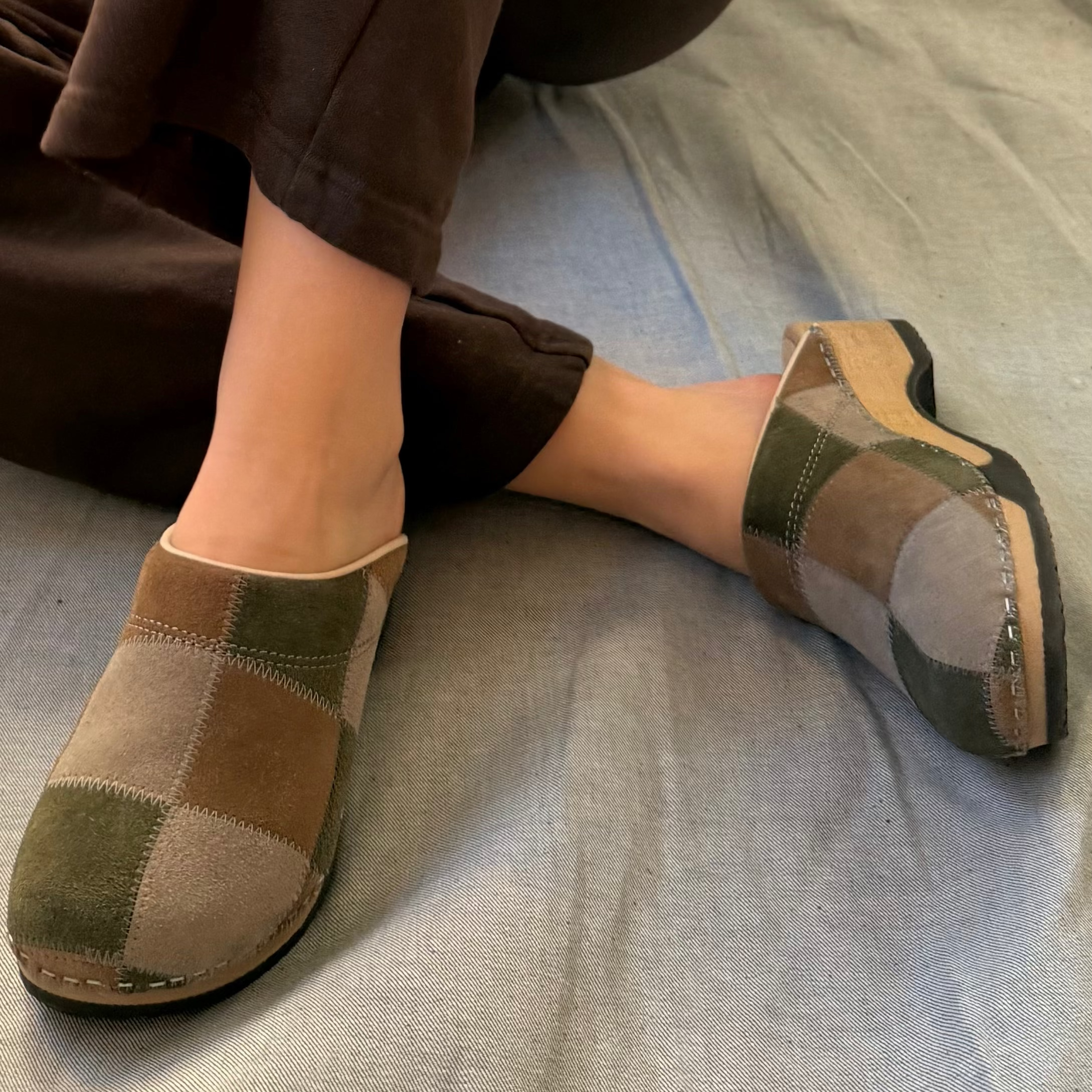 Person wearing brown and green patchwork clogs on a gray surface