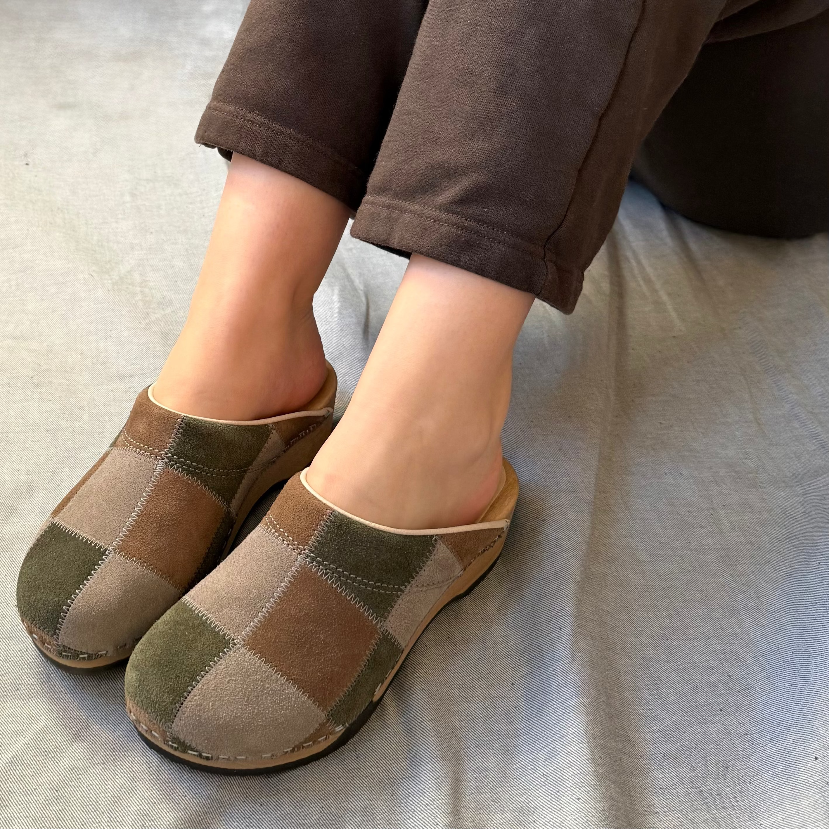 Pair of checkered clogs worn with brown pants on a light gray surface.
